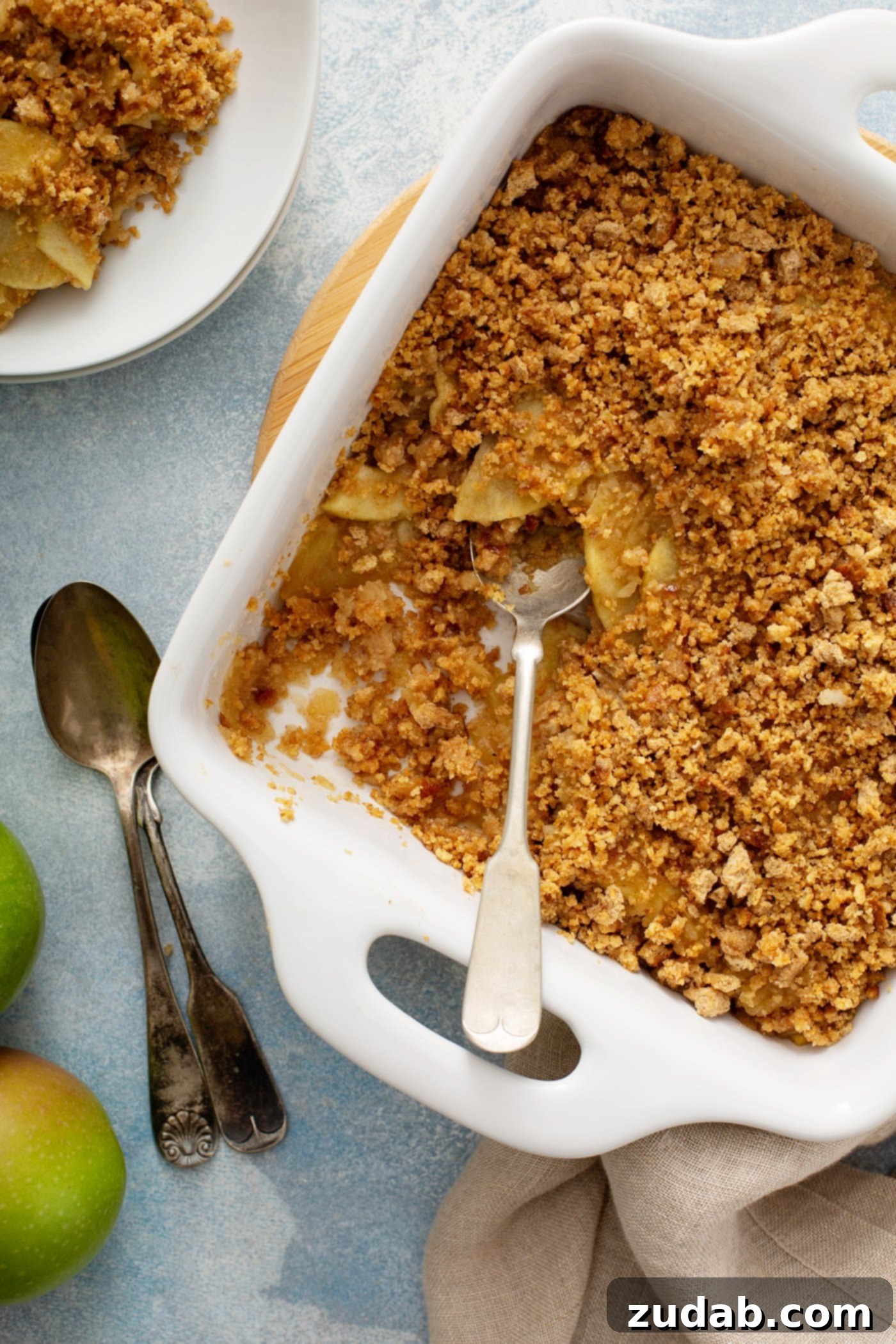 Apple Brown Betty A serving dish filled with warm Apple Brown Betty, featuring tender spiced apples beneath a crispy brown bread crumb topping, ready to be enjoyed. A serving spoon is in the dish, with individual dessert portions in the background.