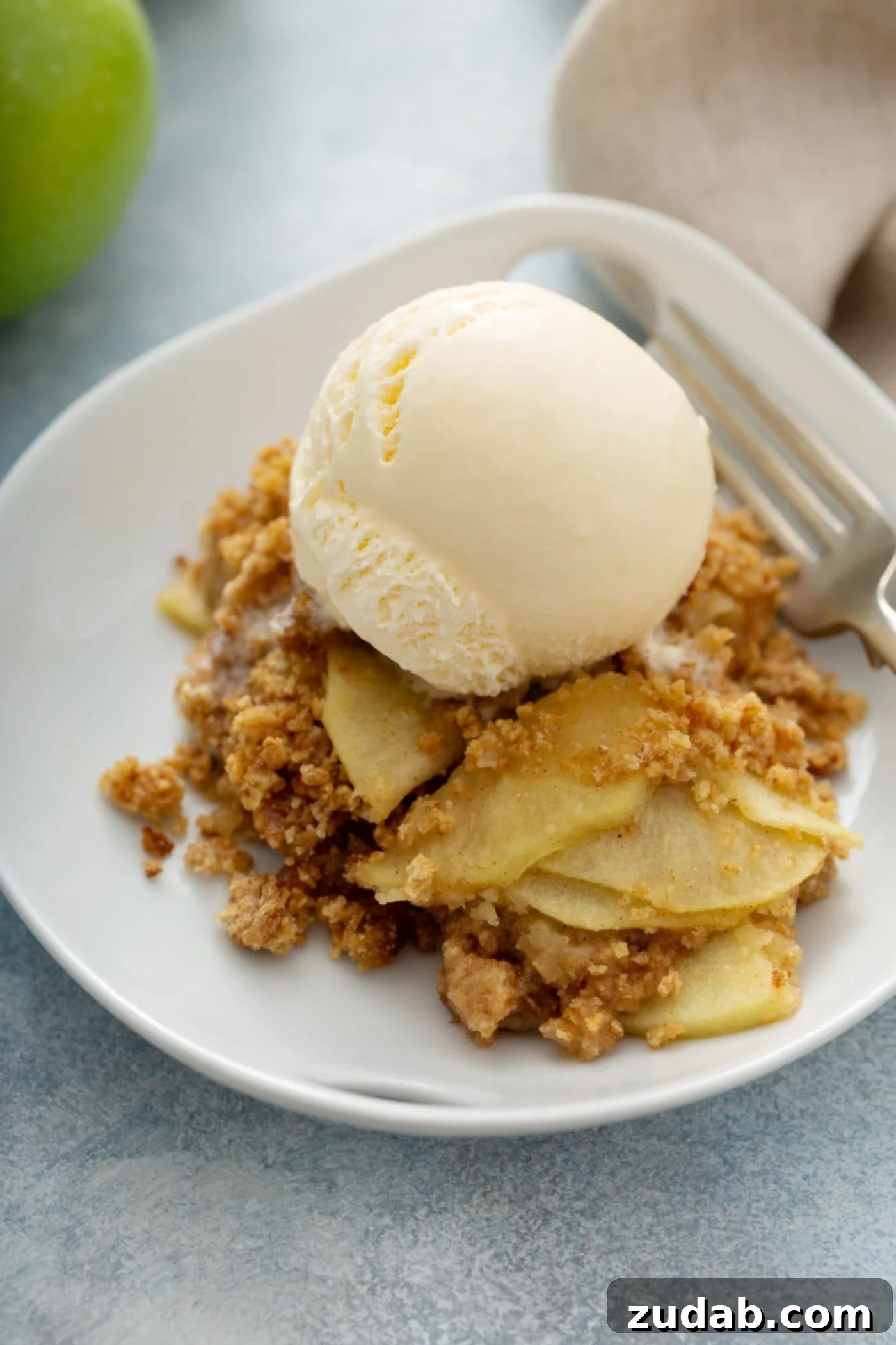Apple Brown Betty A single serving of Apple Brown Betty on a dessert plate, topped with a scoop of ice cream, with a fork resting beside it. This enticing dessert offers a comforting blend of spiced apples and a crispy, buttery bread crumb topping.