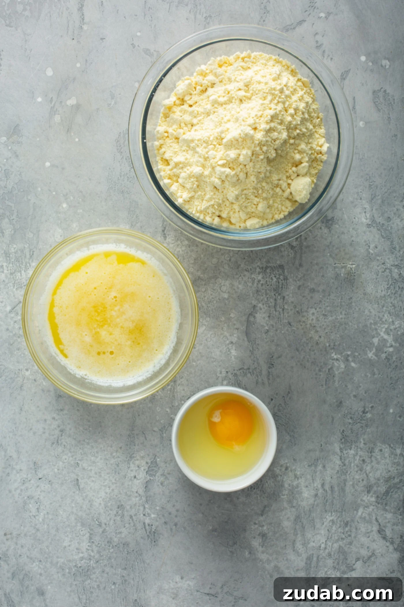 Paula Deen's Pumpkin Gooey Butter Cake Ingredients A table showing three bowls containing cake mix, melted butter, and a single egg out of its shell, ready for mixing.