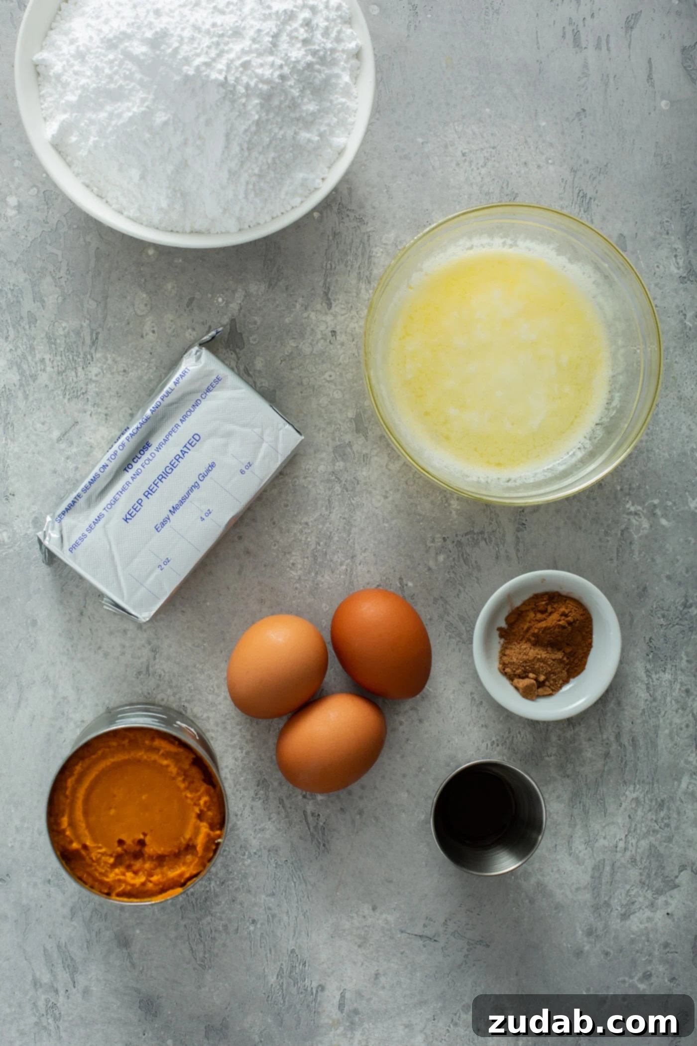 Pumpkin Gooey Butter Cake Ingredients Spread Ingredients for pumpkin gooey butter cake, including bowls of cake mix, melted butter, cinnamon, vanilla, eggs, and a can of pumpkin puree.