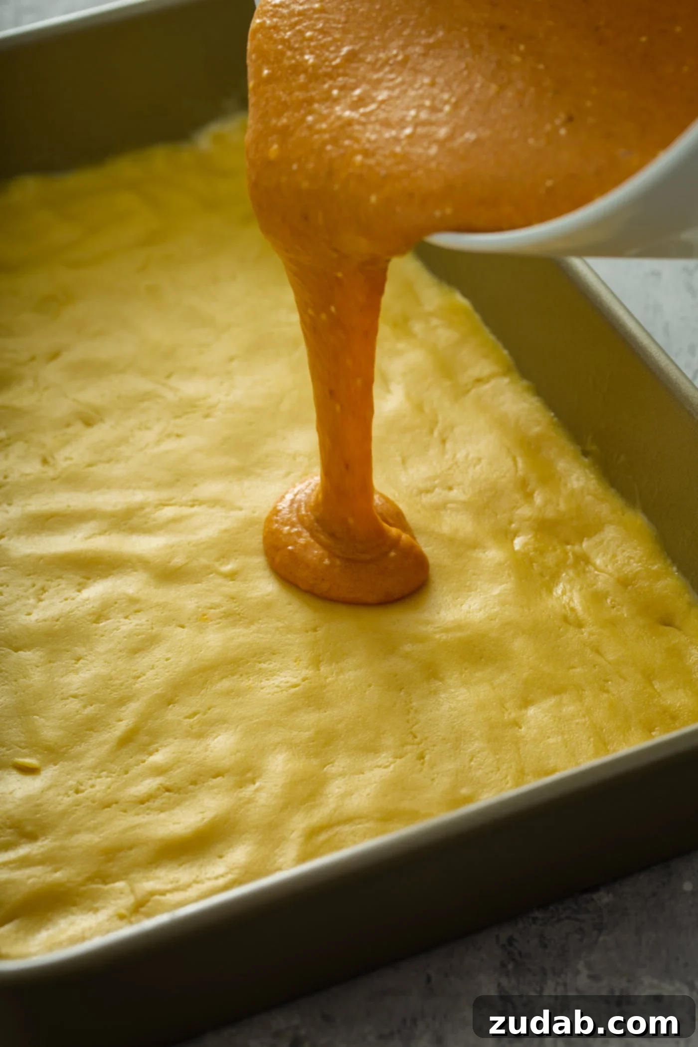 Pouring Pumpkin Mixture on Cake Crust Pumpkin mixture being smoothly poured over a yellow cake mix crust in a baking pan.