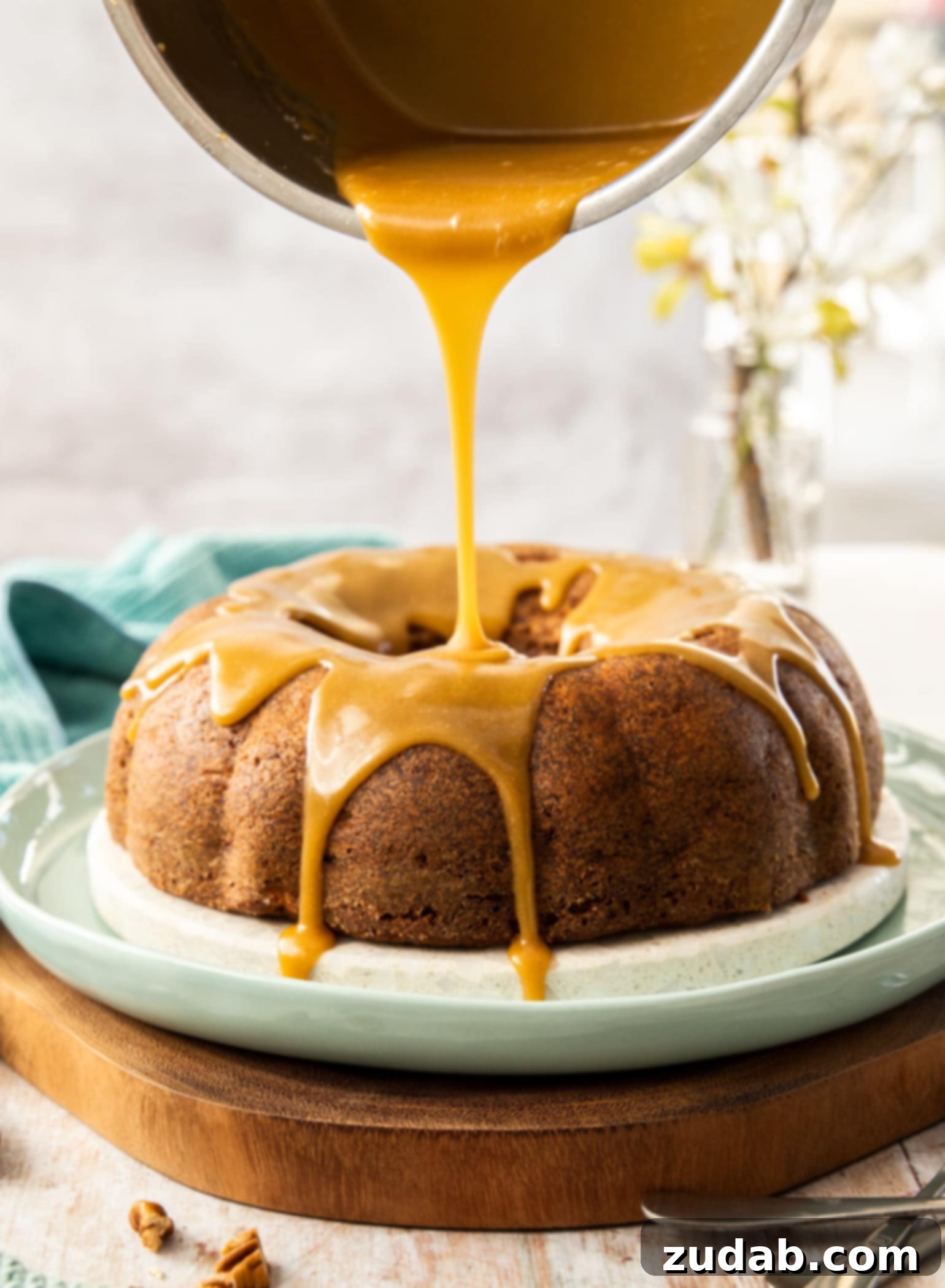 Spiced Apple Pecan Bundt 6 Caramel sauce being poured from a saucepan onto an apple cinnamon bundt cake.