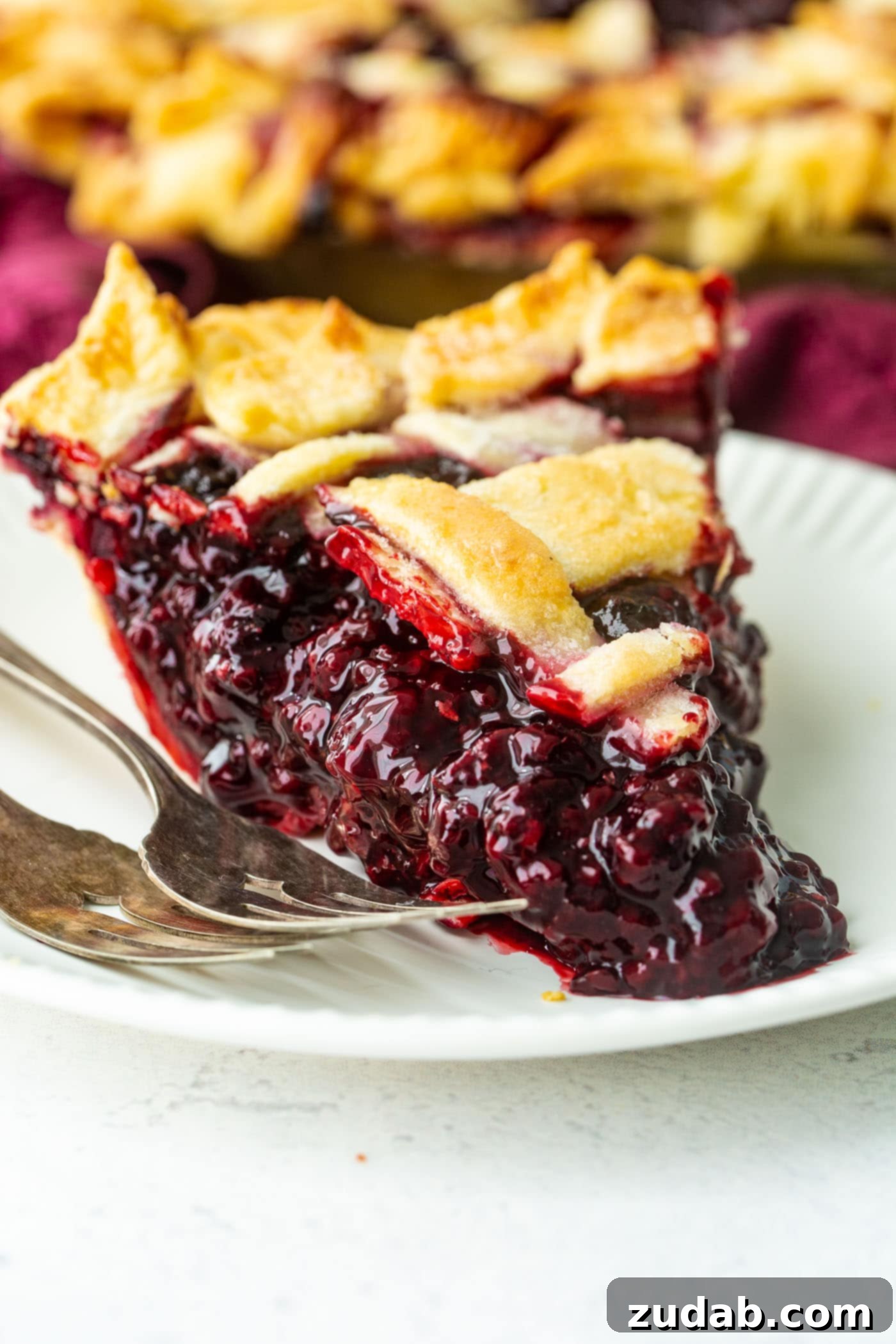 Blackberry Marionberry Pie Perfection 2 A glistening slice of Marionberry pie, perfectly browned crust, nestled on a white plate alongside two elegant forks.