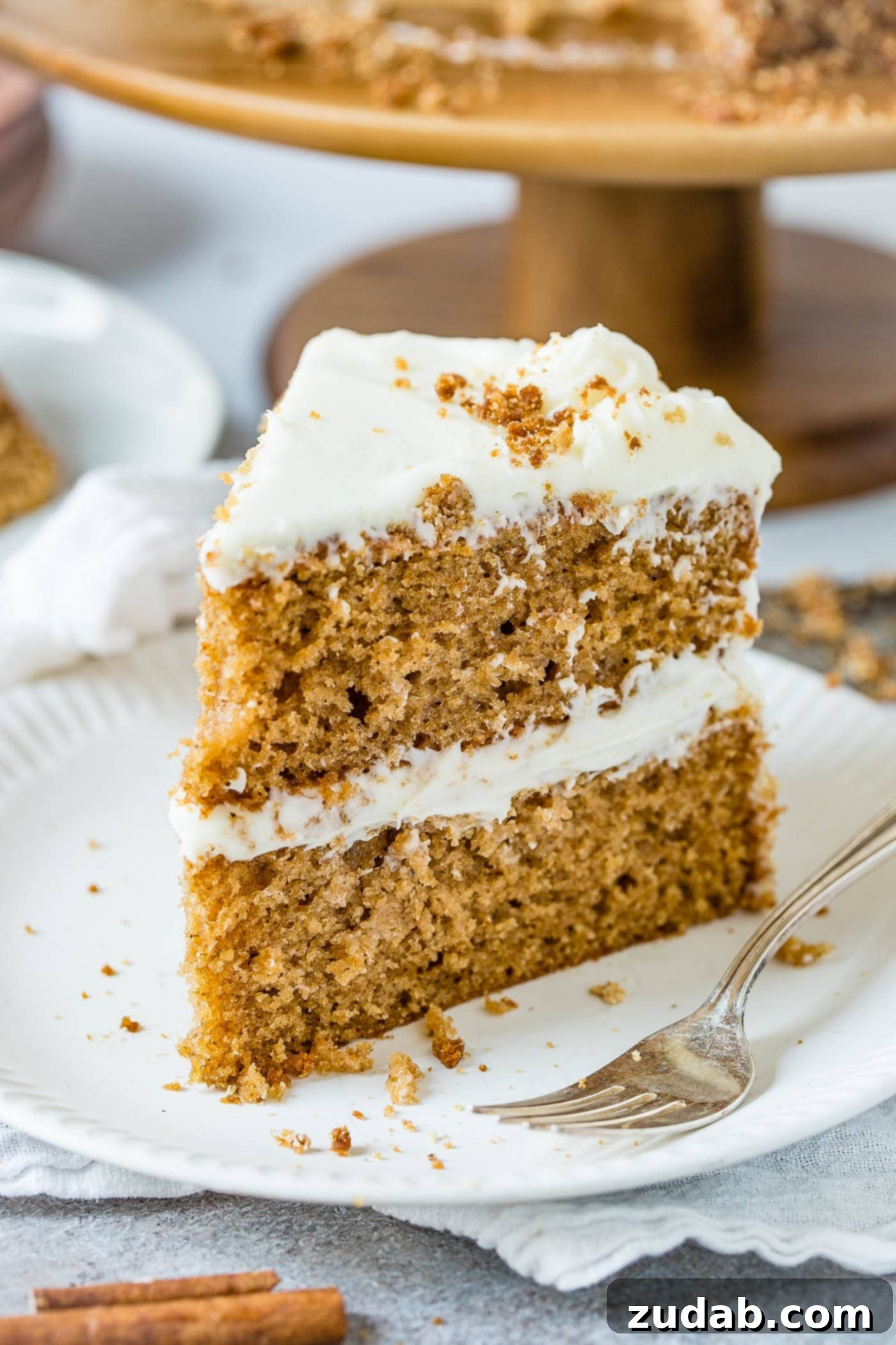 Spice Cake Slice on Plate A perfectly portioned slice of two-layer spice cake adorned with creamy cream cheese frosting, presented on a white dessert plate with a fork beside it.