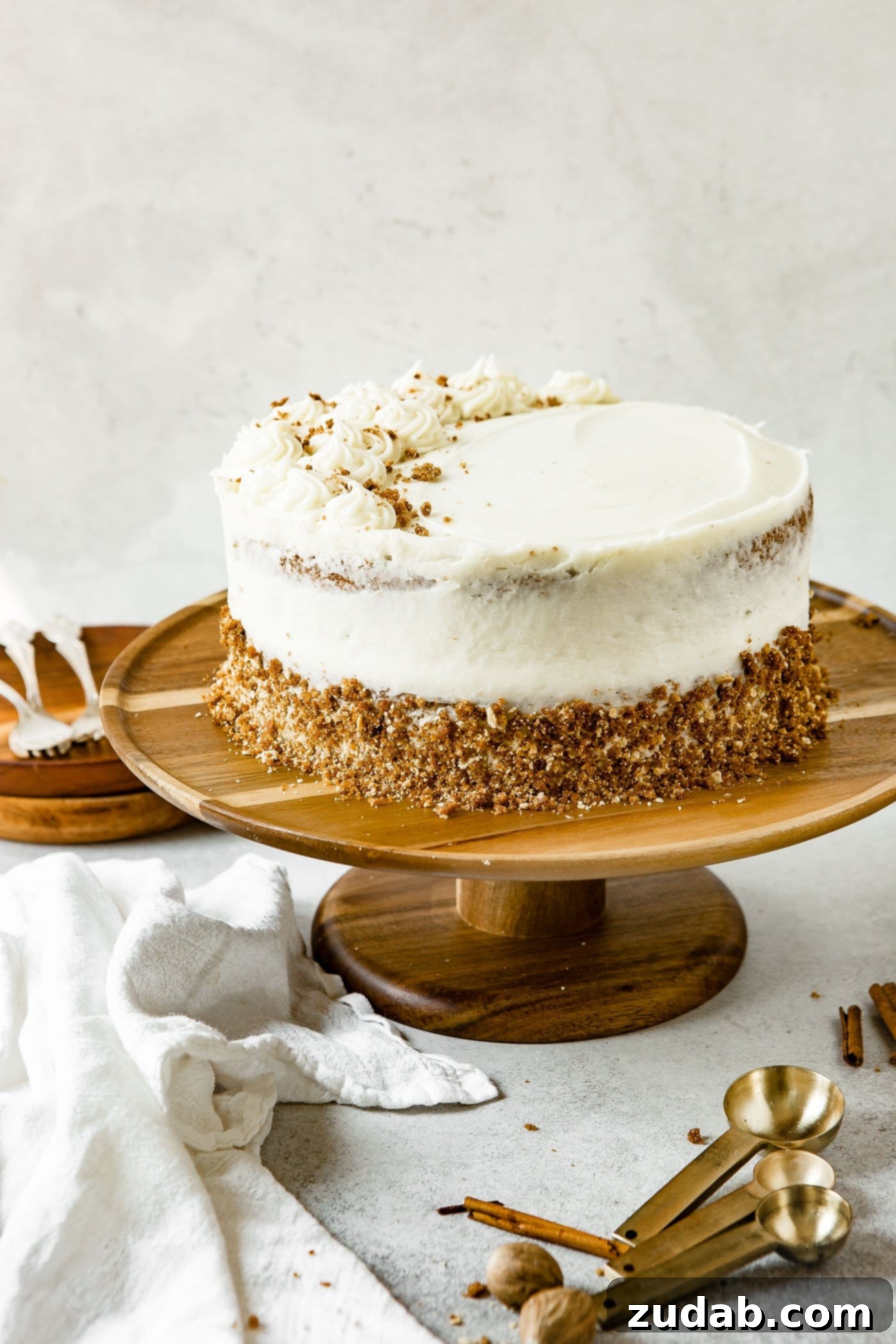 Decorated Spice Cake A two-layered spice cake sitting on a decorative cake stand. The cake is frosted with cream cheese frosting, and the bottom layer's edge is adorned with a delicate crumb mixture, creating a sophisticated rustic look.