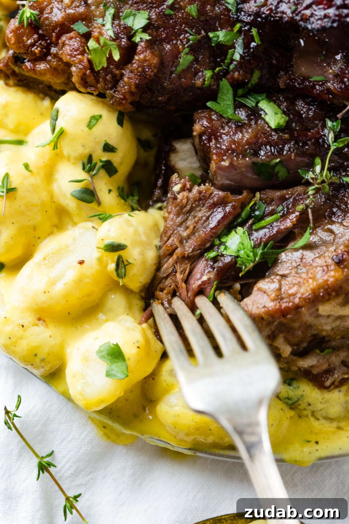 Beef Ribs with Charred Pepper Cream Sauce Gnocchi A close-up shot of fork diving into a plate of oven braised short ribs and creamy gnocchi, highlighting the perfect texture.