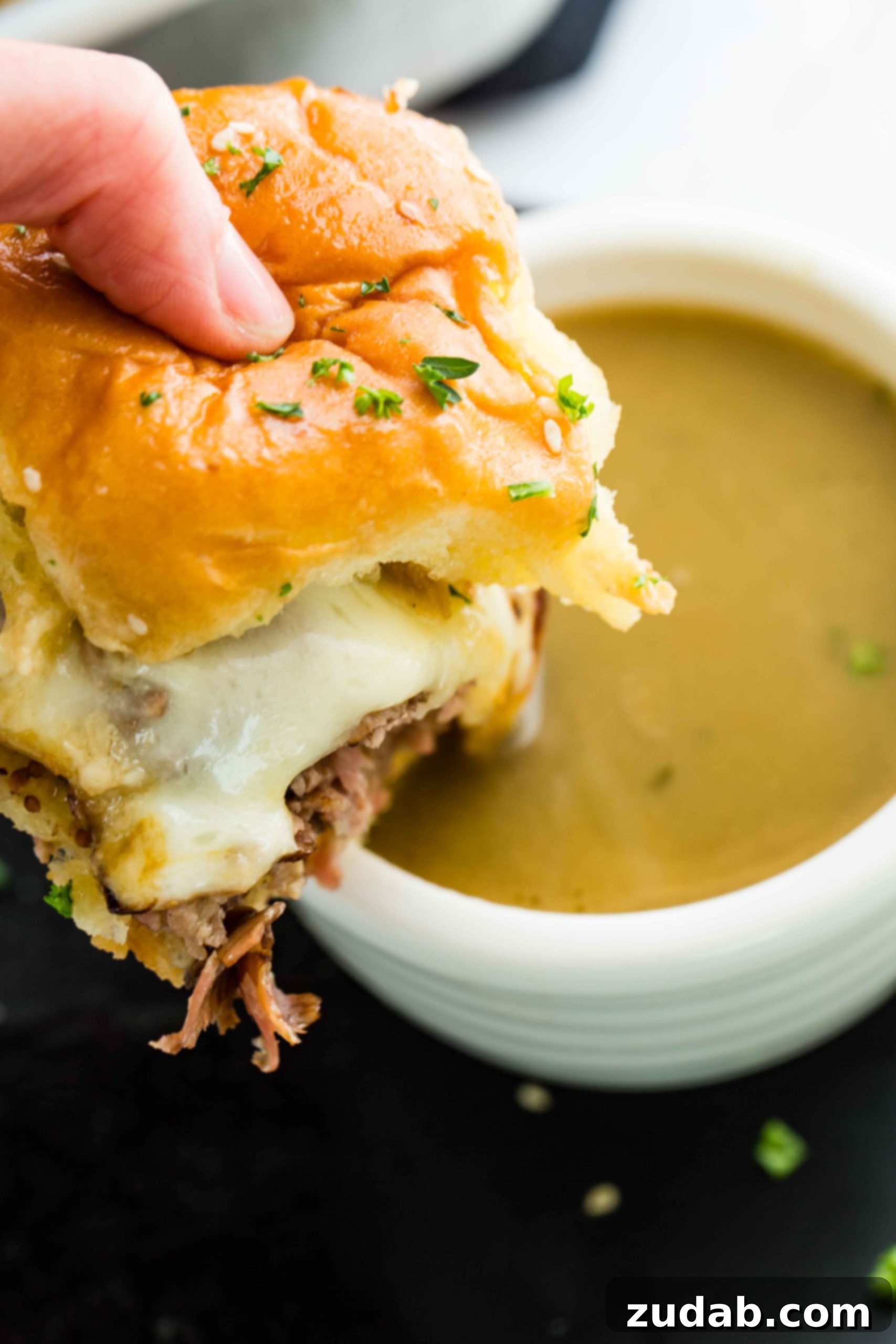 French Dip Sliders 4 A photo of someone holding a single french dip slider about to dip it into a cup of aus jus.