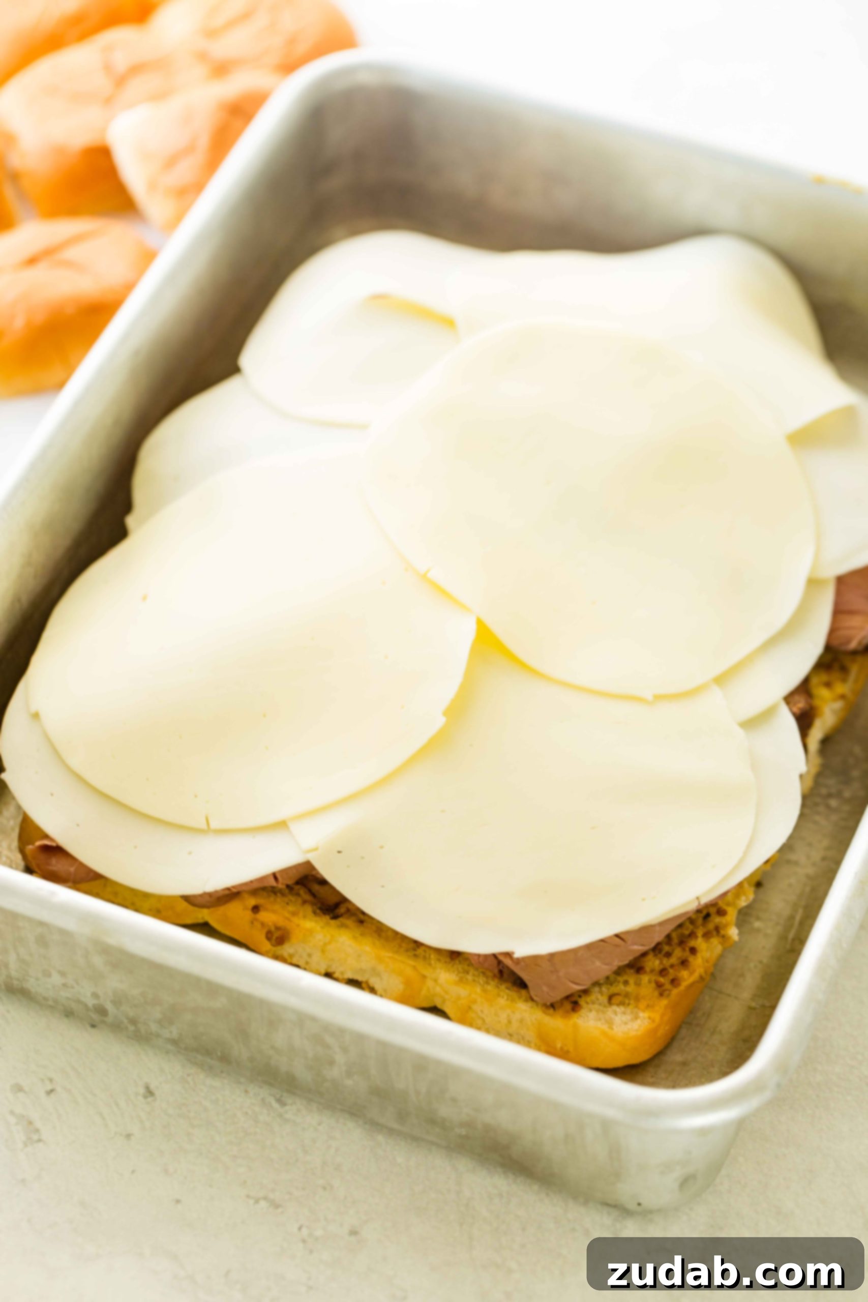 French Dip Sliders A photo of french dip sliders being constructed with a layer of provolone added on tope of the roast beef.