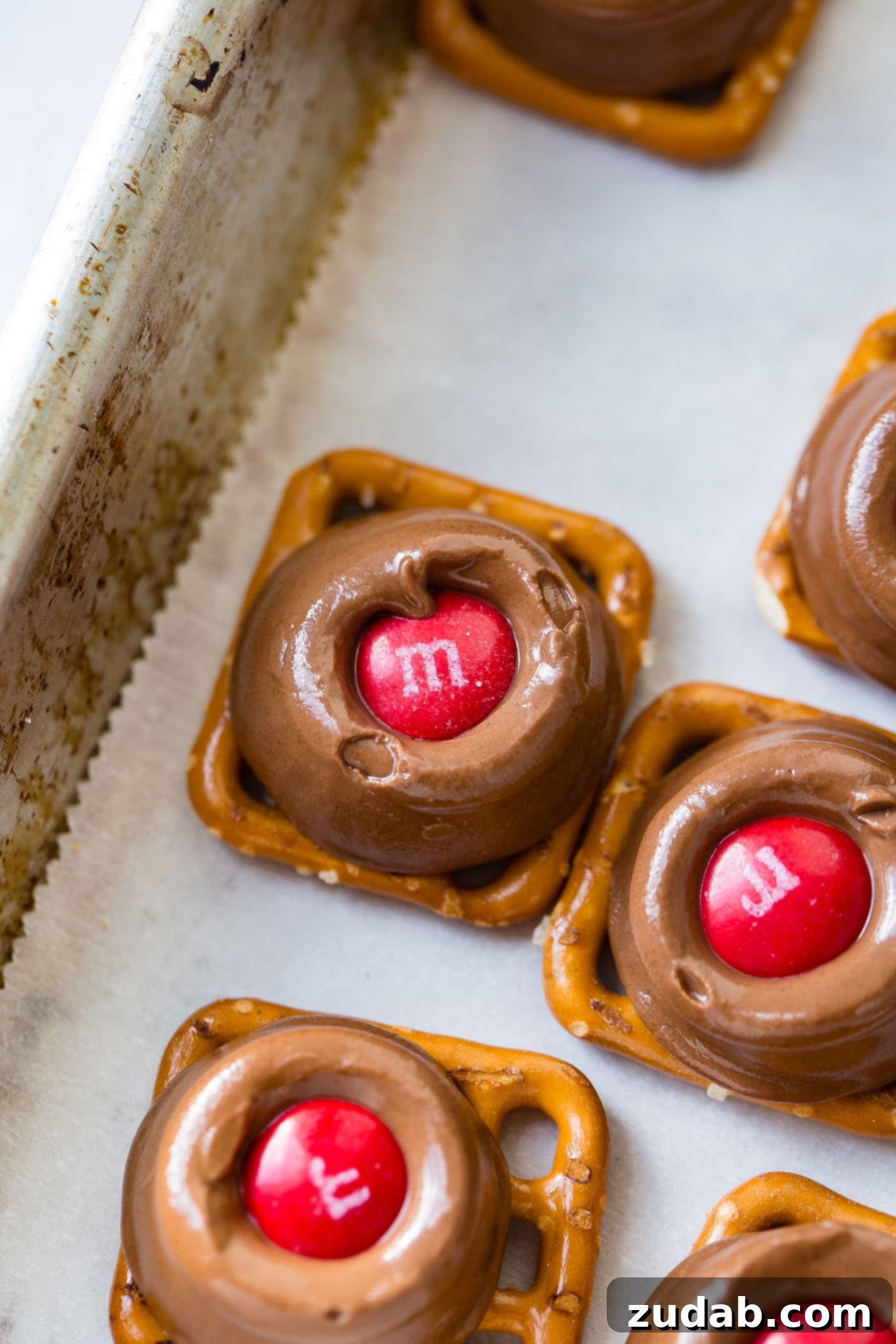 Rolo Pretzels with M&Ms A platter with Rolo pretzels topped with vibrant red and green M&Ms, arranged on parchment paper, ready for holiday serving.