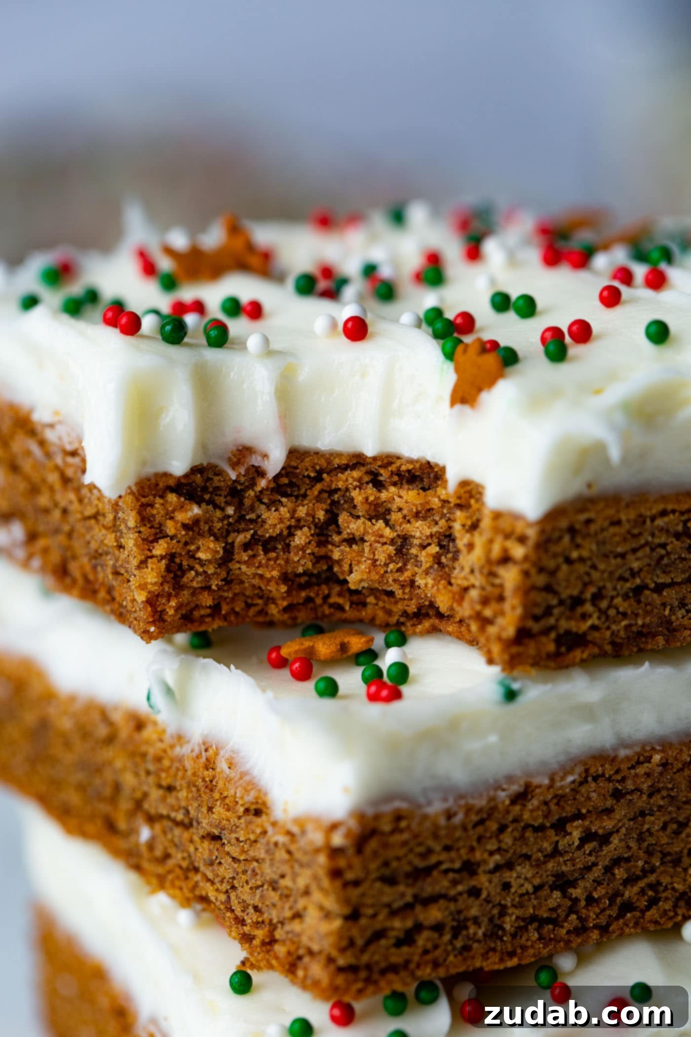 Gingerbread Bars with Cream Cheese Frosting A stack of three gingerbread bars, each generously frosted with cream cheese frosting, with a delightful bite taken from the top bar, showcasing its soft interior.