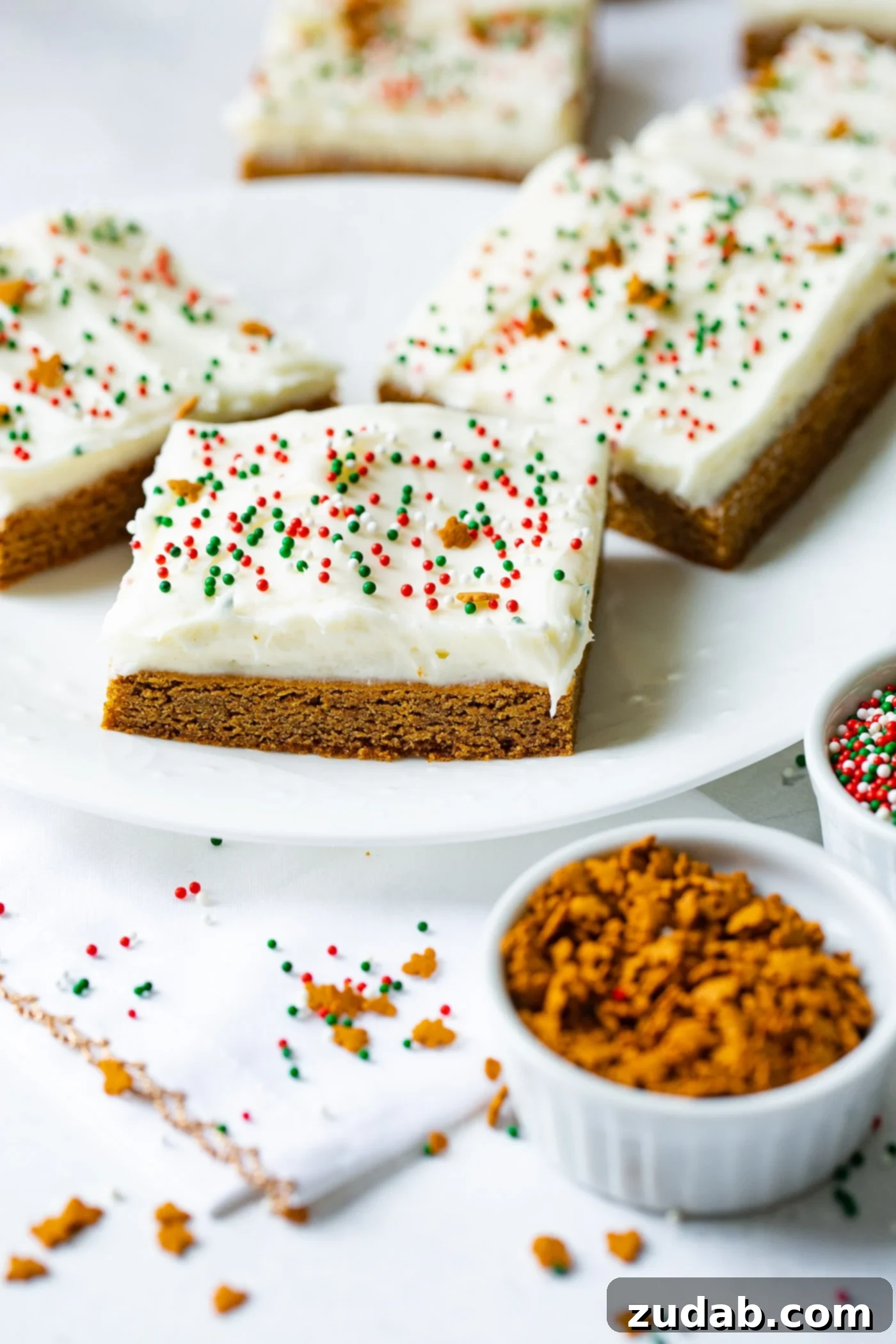 Gingerbread Bars with Cream Cheese Frosting A festive arrangement of gingerbread bars on a white plate, complete with swirls of cream cheese frosting and colorful holiday sprinkles, ready to be enjoyed.