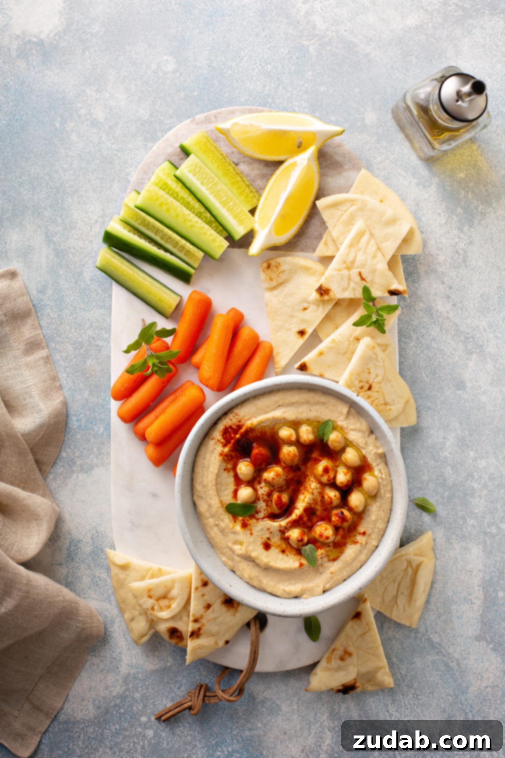 Hummus Dipping Platter A beautifully arranged tray featuring a bowl of homemade hummus, topped with whole chickpeas and smoked paprika, flanked by fresh baby carrots, crisp celery sticks, bright lemon wedges, and crunchy tortilla wedges.
