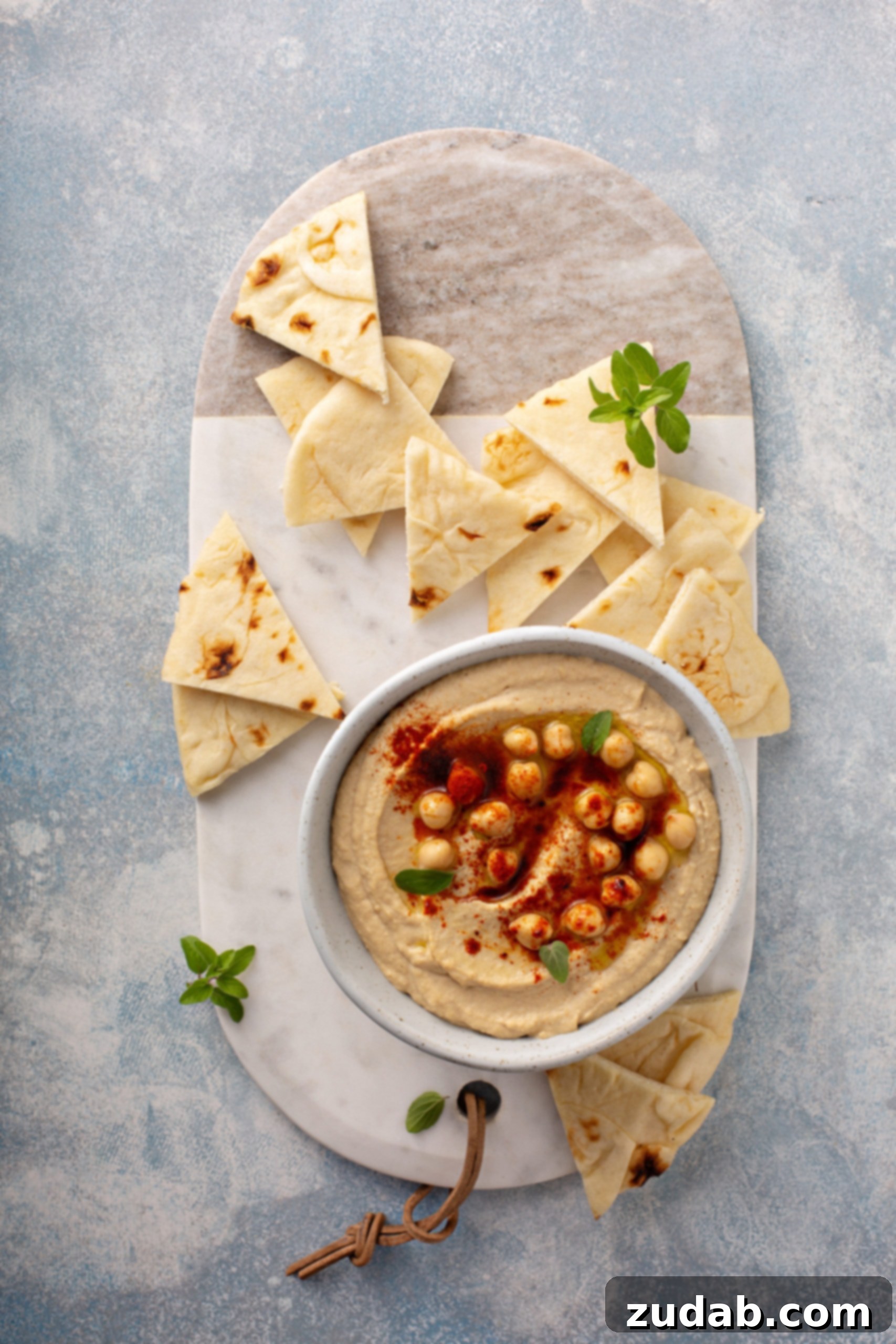 Healthy Homemade Hummus A close-up of a bowl of homemade hummus, beautifully garnished with whole chickpeas and a sprinkle of smoked paprika, with tortilla wedges arranged enticingly in the background.