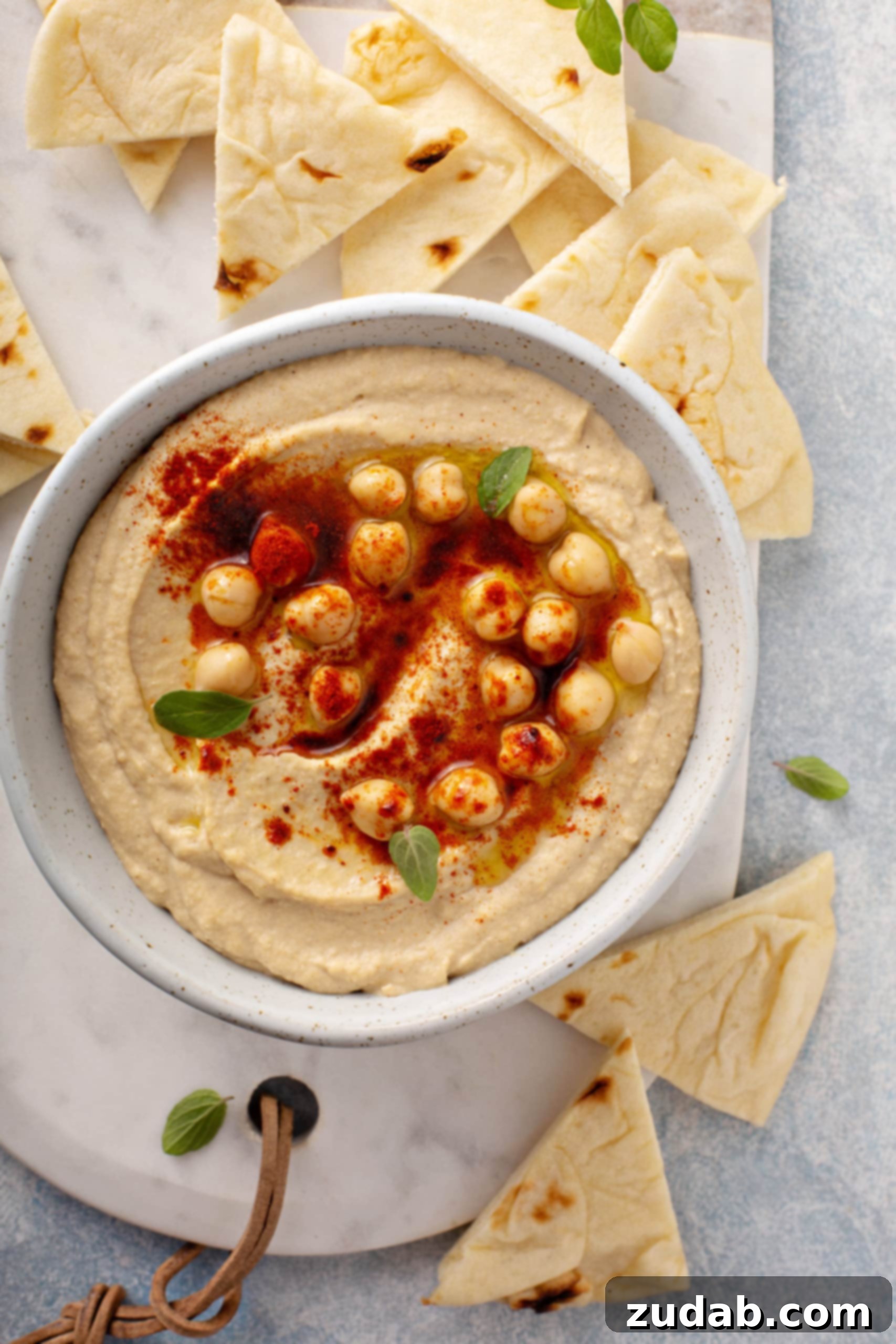 Perfectly Creamy Hummus An inviting close-up of a bowl of exceptionally creamy hummus, richly topped with whole chickpeas and a delicate dusting of smoked paprika, surrounded by a border of crisp flour tortilla wedges.