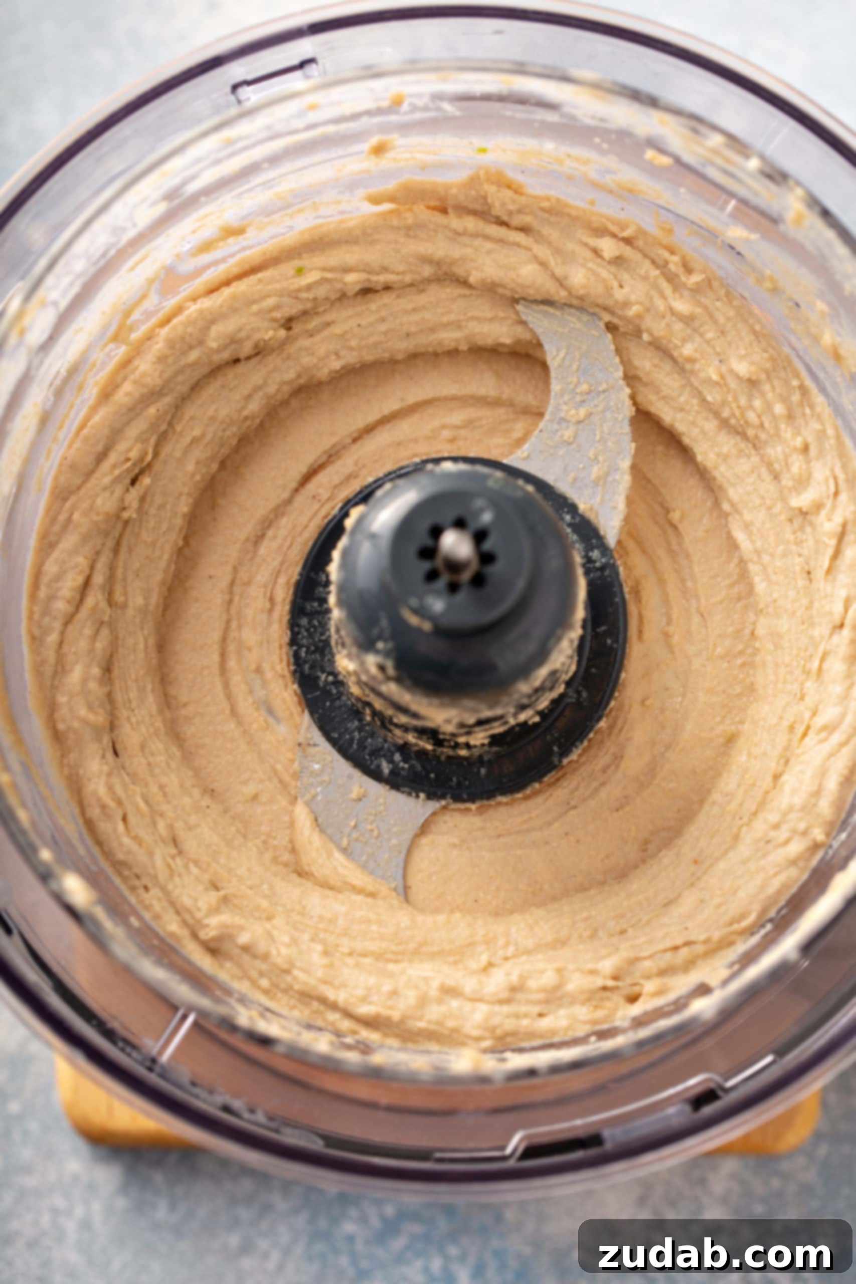 Tahini Blending for Hummus The food processor bowl now holds a creamy, pale mixture of lemon, garlic, salt, and tahini, blended to perfection for homemade hummus.
