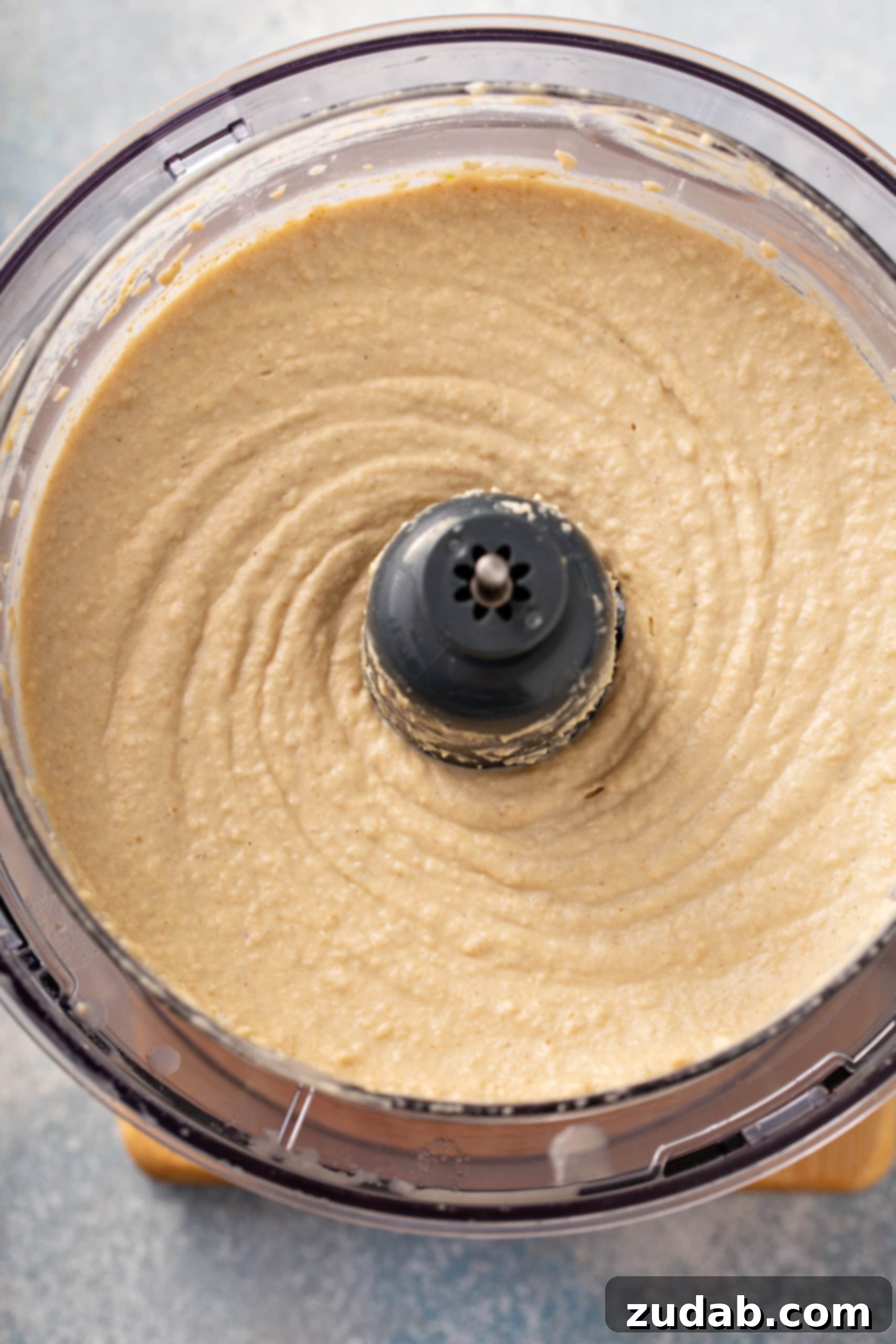 Creamy Hummus in Food Processor The food processor now contains perfectly smooth, pale, and creamy hummus, a testament to proper blending and the addition of ice water.