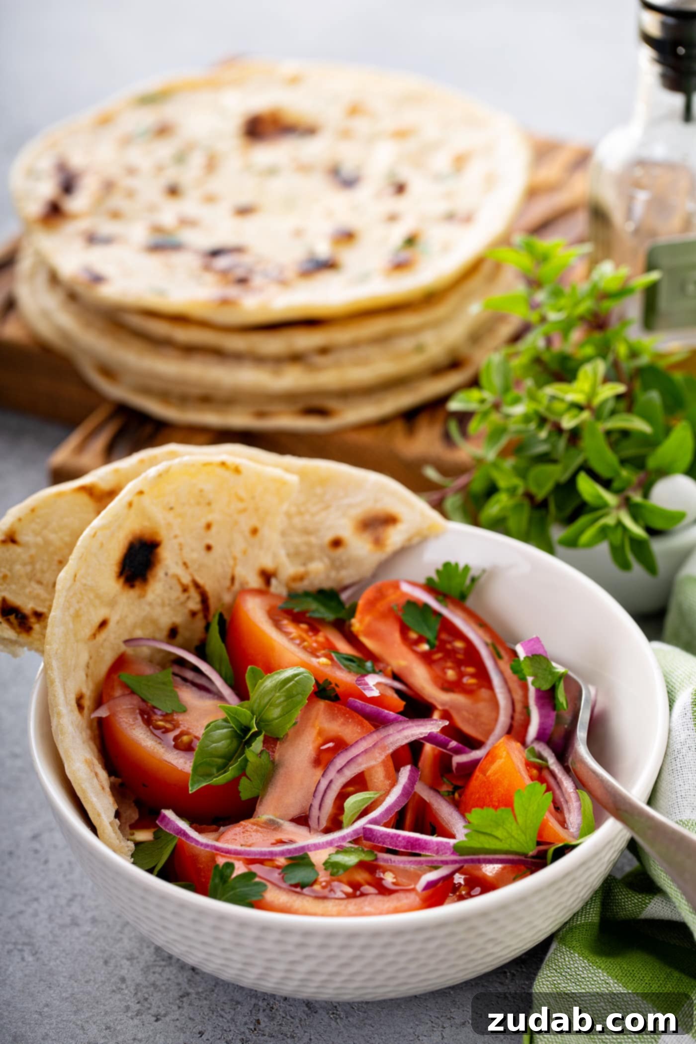 Unleavened Bread A photo of a bowl of fresh tomato and onion salad in a white bowl with torn pieces of unleavened bread sitting on the side of the bowl and a stack of bread in the background.