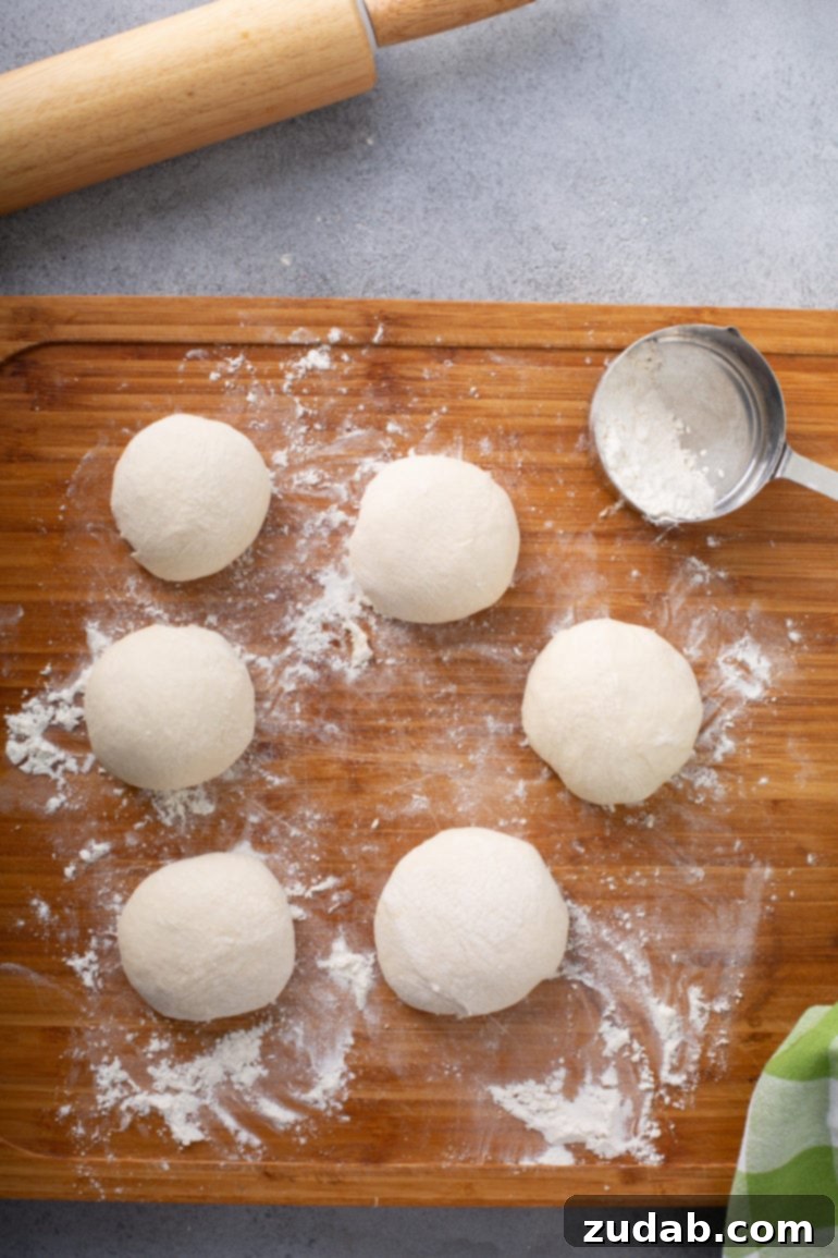 Whip Up Three Ingredient Unleavened Bread 3 A photo of six blobs of unleavened bread dough sitting on a floured wooden cutting board with a measuring cup of flour sitting next to them.