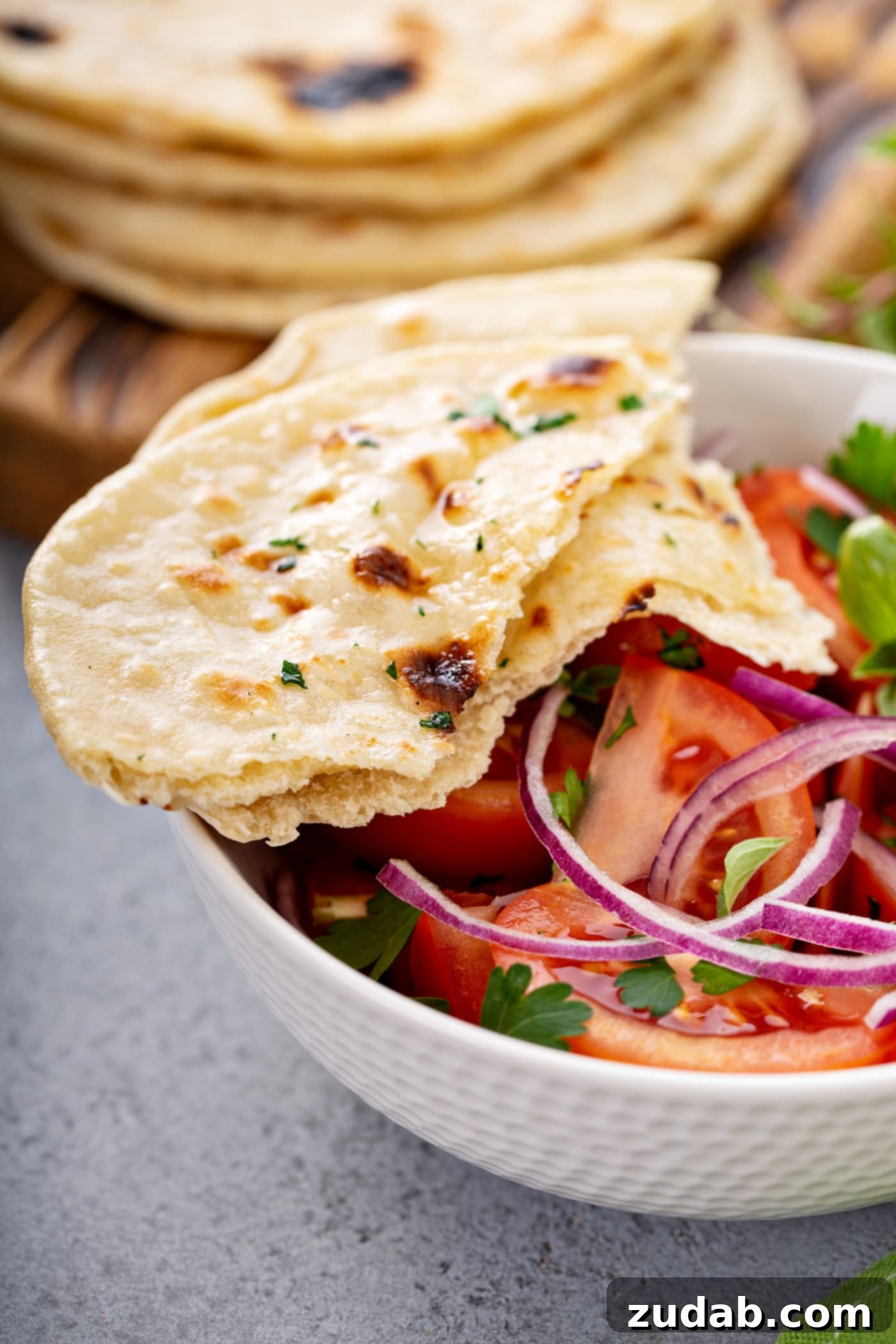 Unleavened Bread A photo of a bowl of fresh tomato and onion salad in a white bowl with torn pieces of flatbread sitting on the side of the bowl.