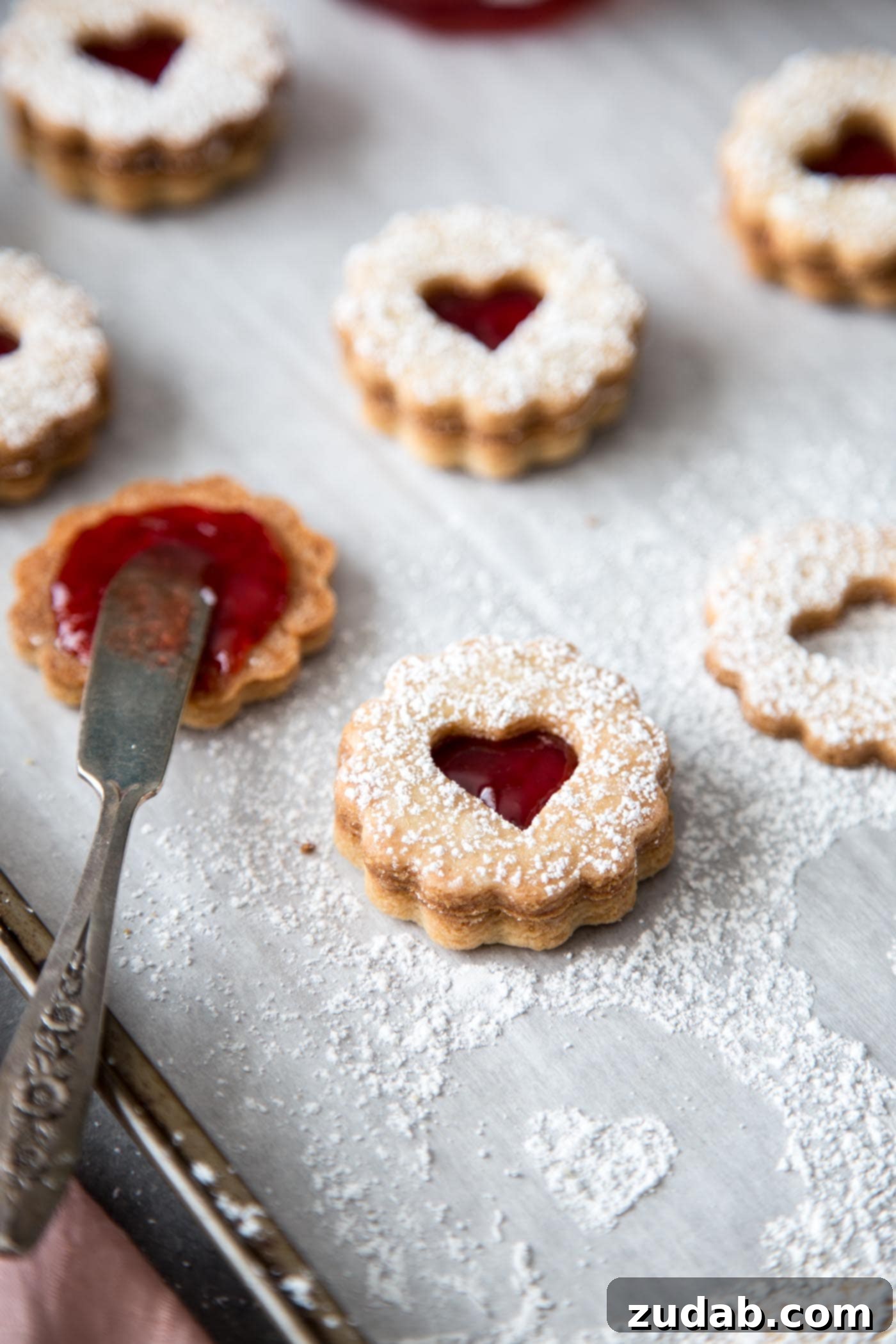 Classic Linzer Cookies 2 Linzer cookies with strawberry jam filling on a baking sheet, ready to be served