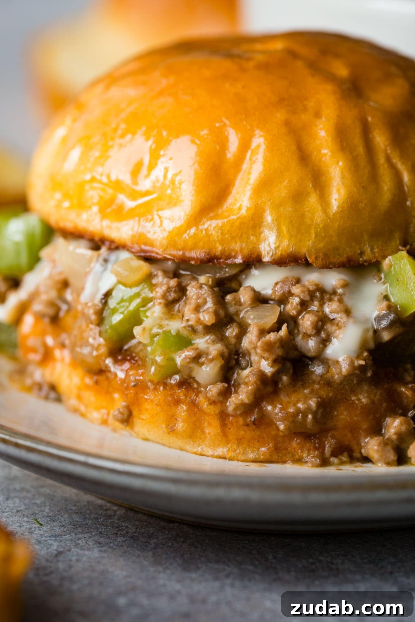Philly Cheesesteak Sloppy Joes A closeup photo of a philly cheesesteak sloppy joe on a toasted brioche bun with melted cheese coming out the sides.