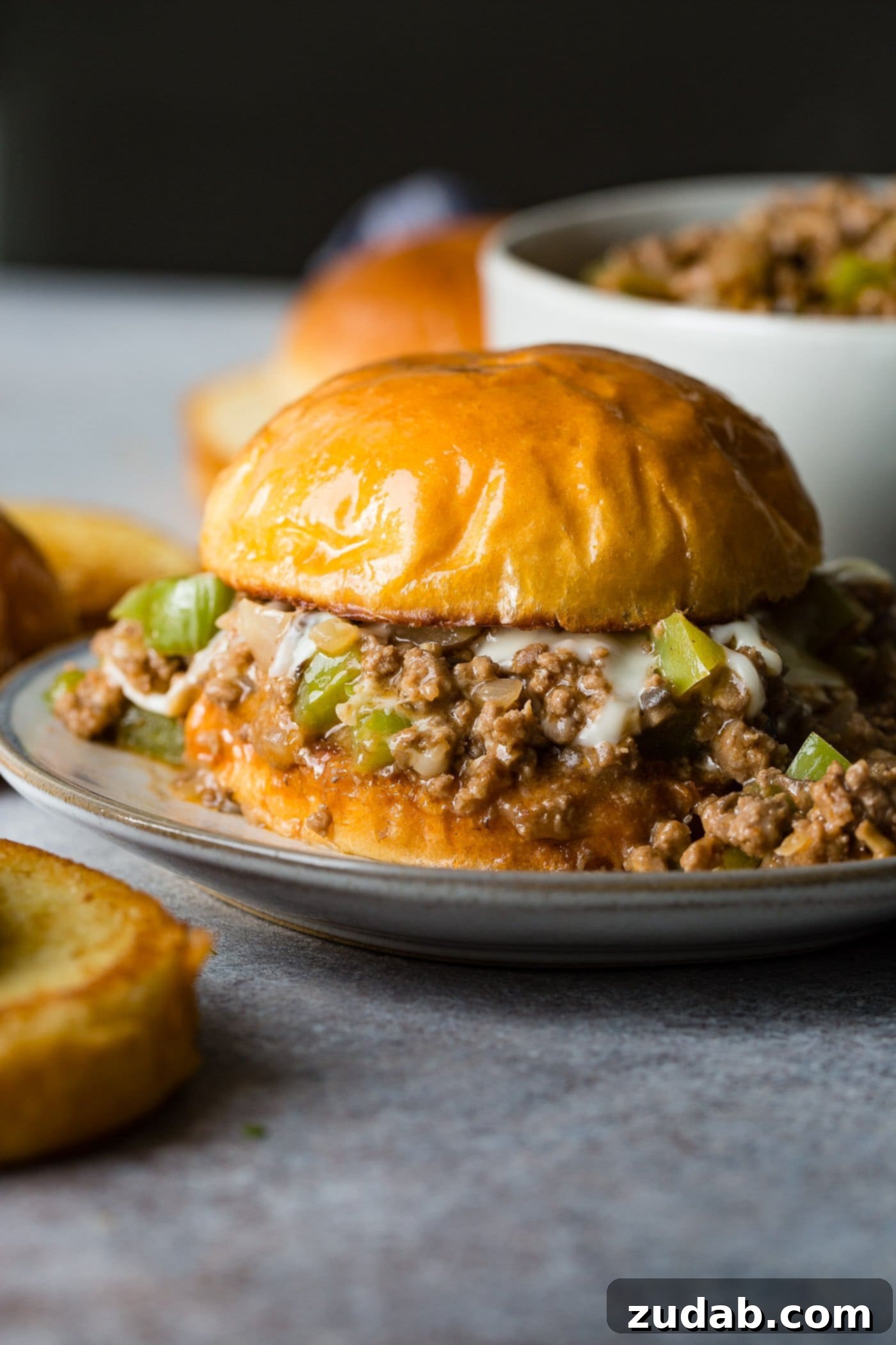 Philly Cheesesteak Sloppy Joes A photo of a philly cheesesteak sloppy joe on a toasted brioche bun on a white plate.