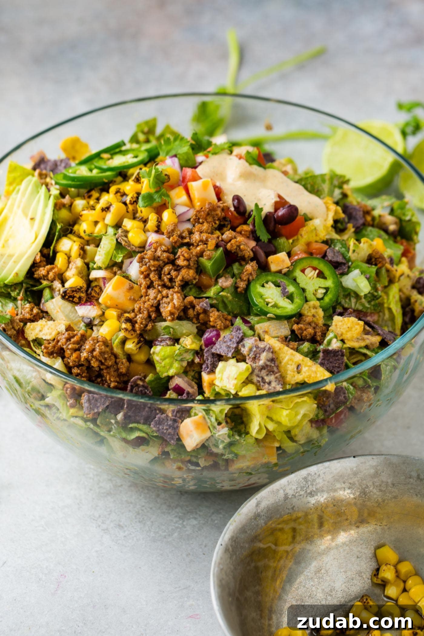 A large glass bowl of vibrant Tex-Mex taco salad filled with colorful ingredients like seasoned ground beef, crisp lettuce, juicy tomatoes, sweet corn, black beans, and crunchy tortilla chips.