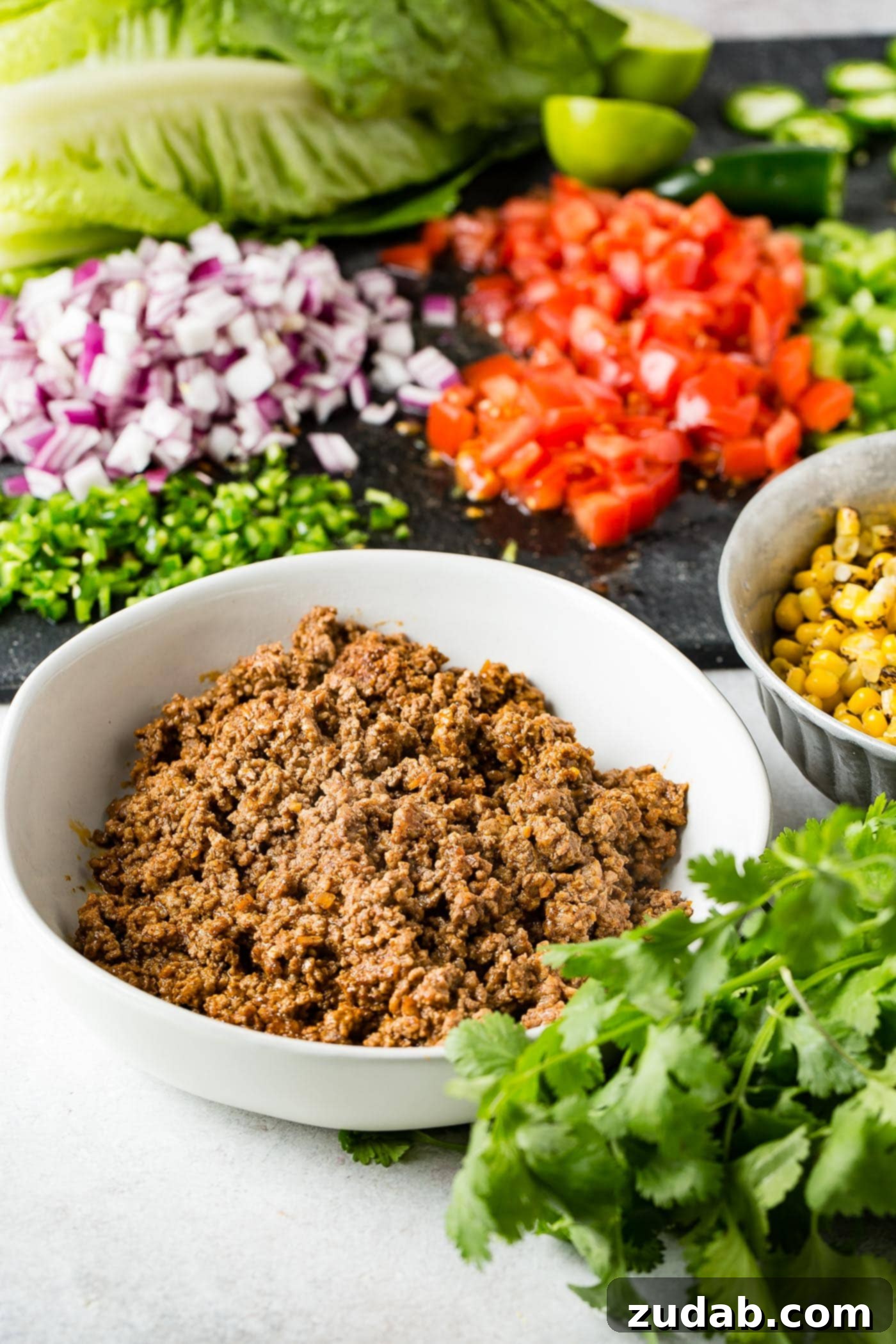 A selection of fresh ingredients for Tex-Mex taco salad, including a bowl of seasoned taco meat, a bowl of roasted corn, fresh cilantro, vibrant chopped green bell peppers, diced tomatoes, and finely chopped red onion.