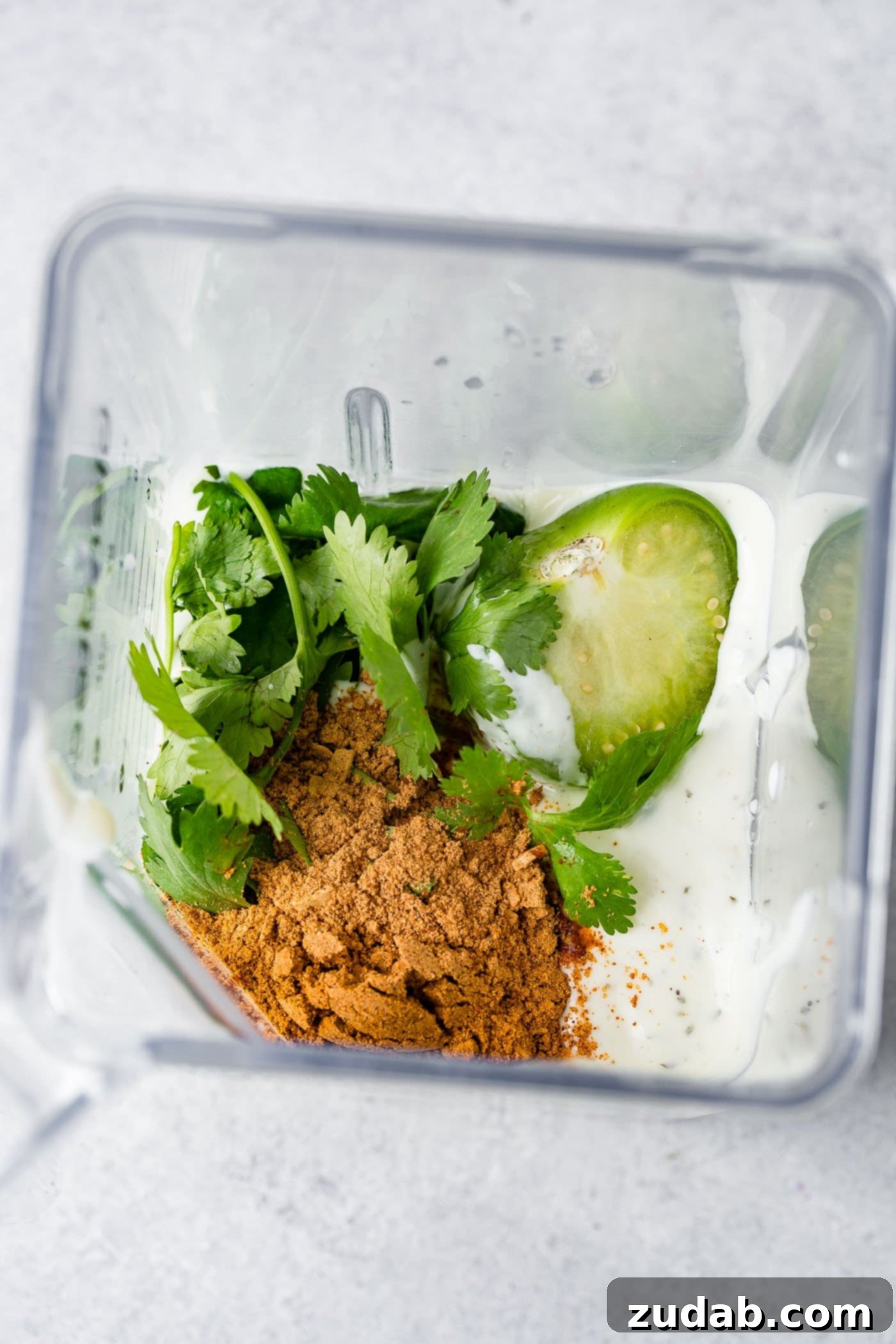 A blender ready with ranch dressing, taco seasoning, cilantro, and tomatillo halves, poised to create a smooth and flavorful taco salad dressing.