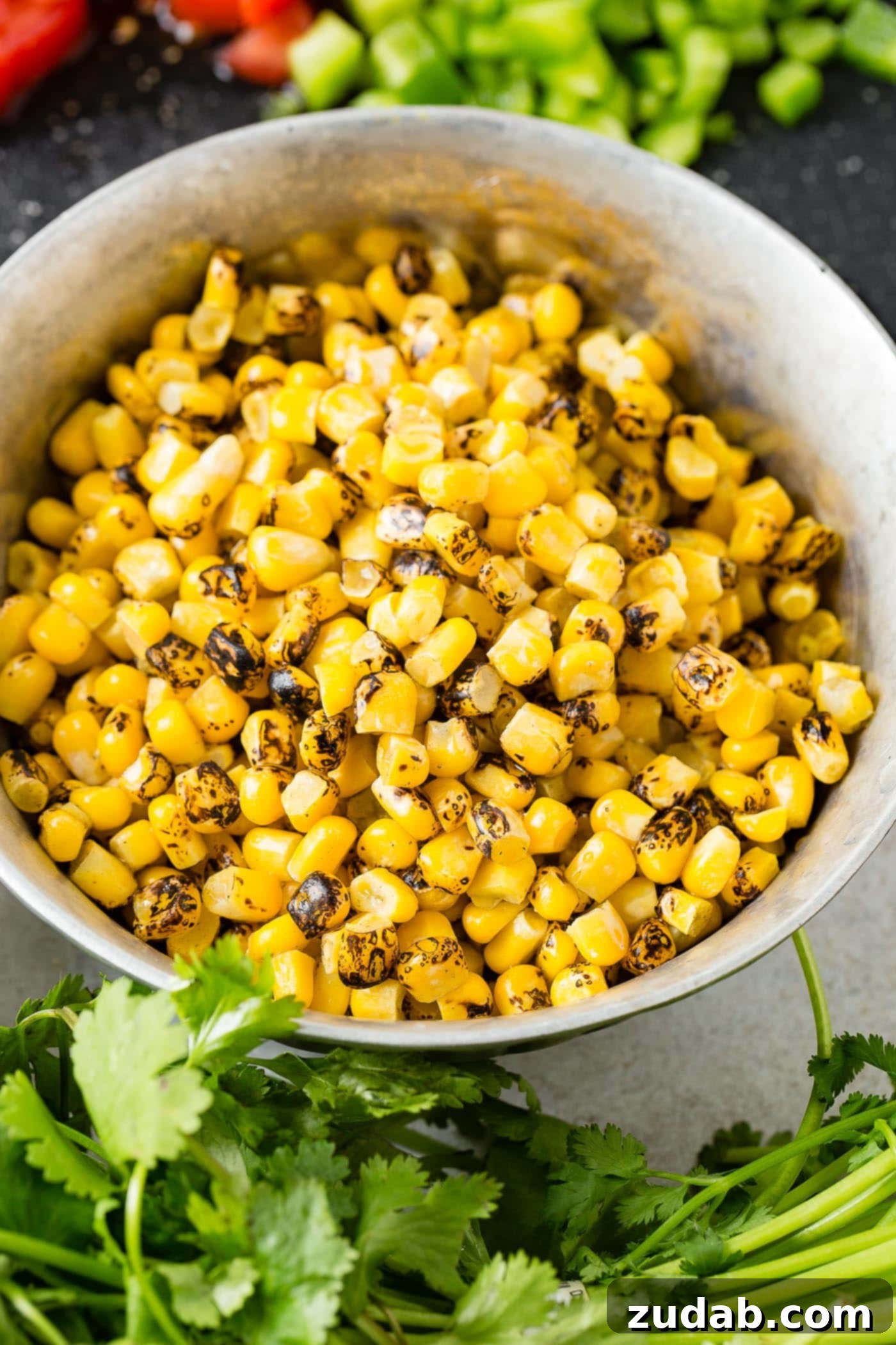 A bowl of roasted corn, beautifully garnished with fresh cilantro leaves, ready to be added to a vibrant Tex-Mex taco salad.
