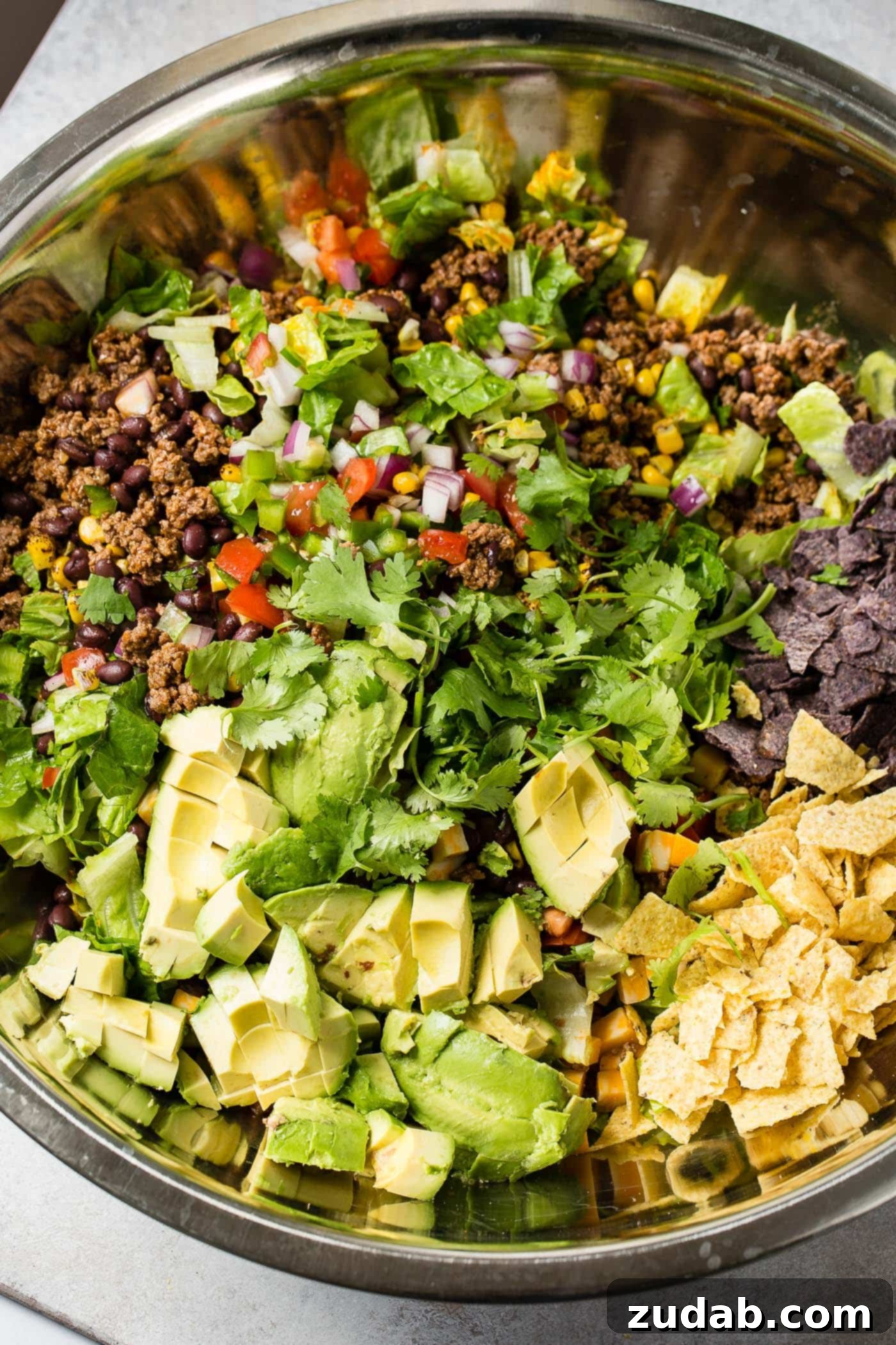 A close-up shot of a vibrant Tex-Mex taco salad, highlighting the fresh, crisp lettuce, juicy diced tomatoes, sweet corn, crunchy tortilla chips, and perfectly seasoned taco meat.