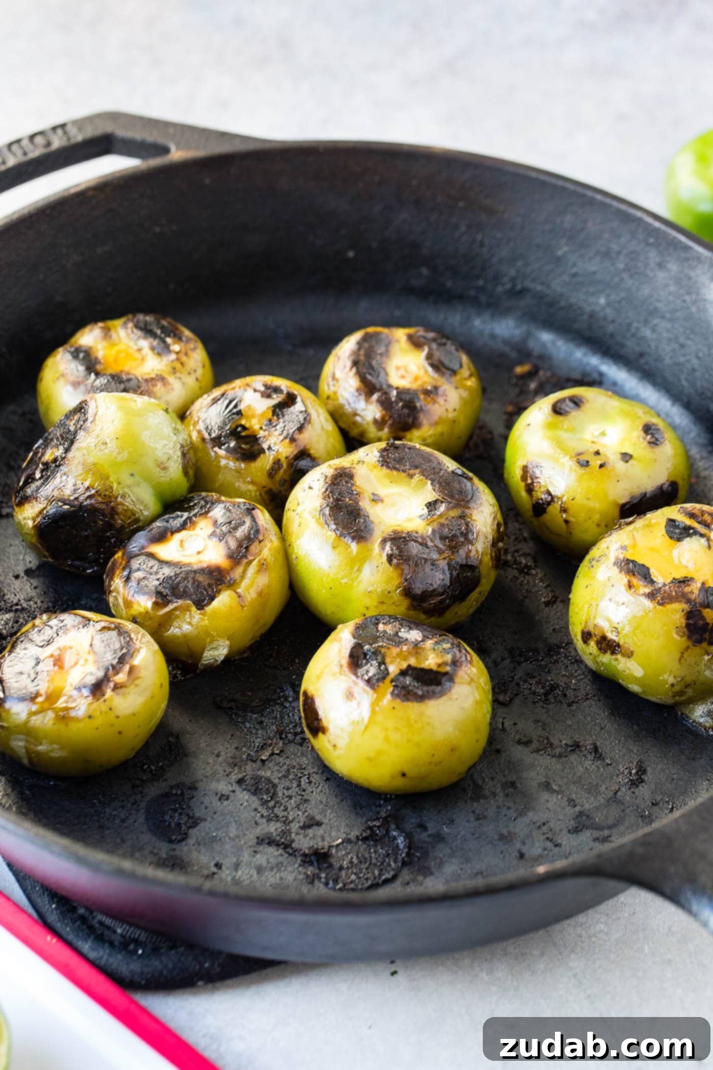 Authentic Salsa Verde From Scratch 4 Nine perfectly roasted tomatillos, showing a slight char, arranged in a rustic cast iron skillet, ready to be transformed into authentic salsa verde.