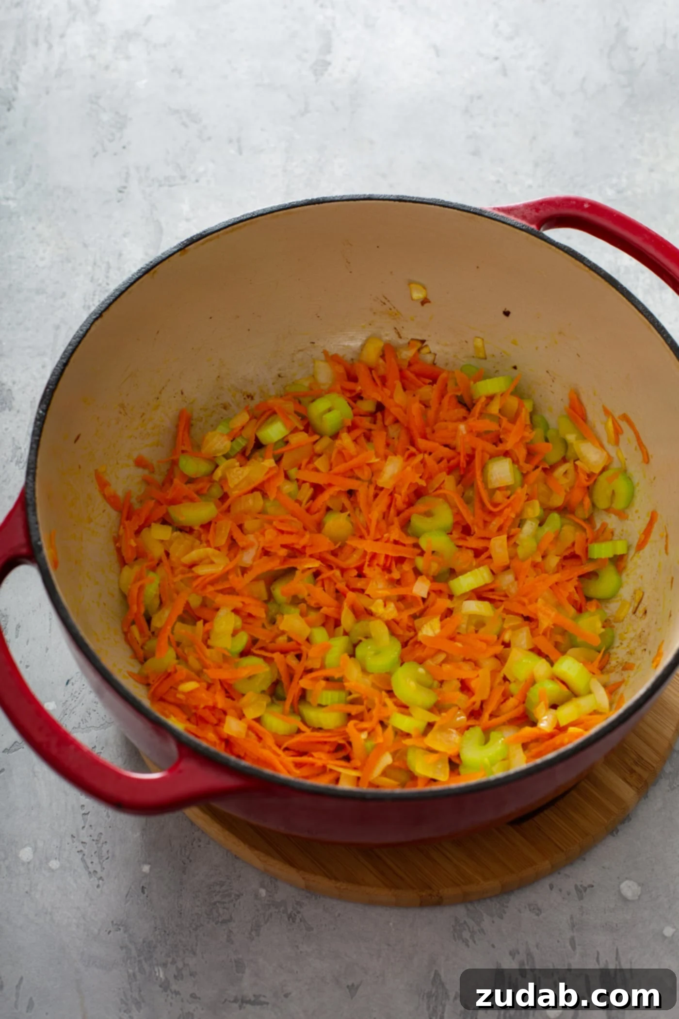 Olive Garden Gnocchi Chicken Soup A red Dutch oven on a stovetop, filled with brightly colored shredded carrots and sliced green celery, sautéing to form the flavor base of the soup.