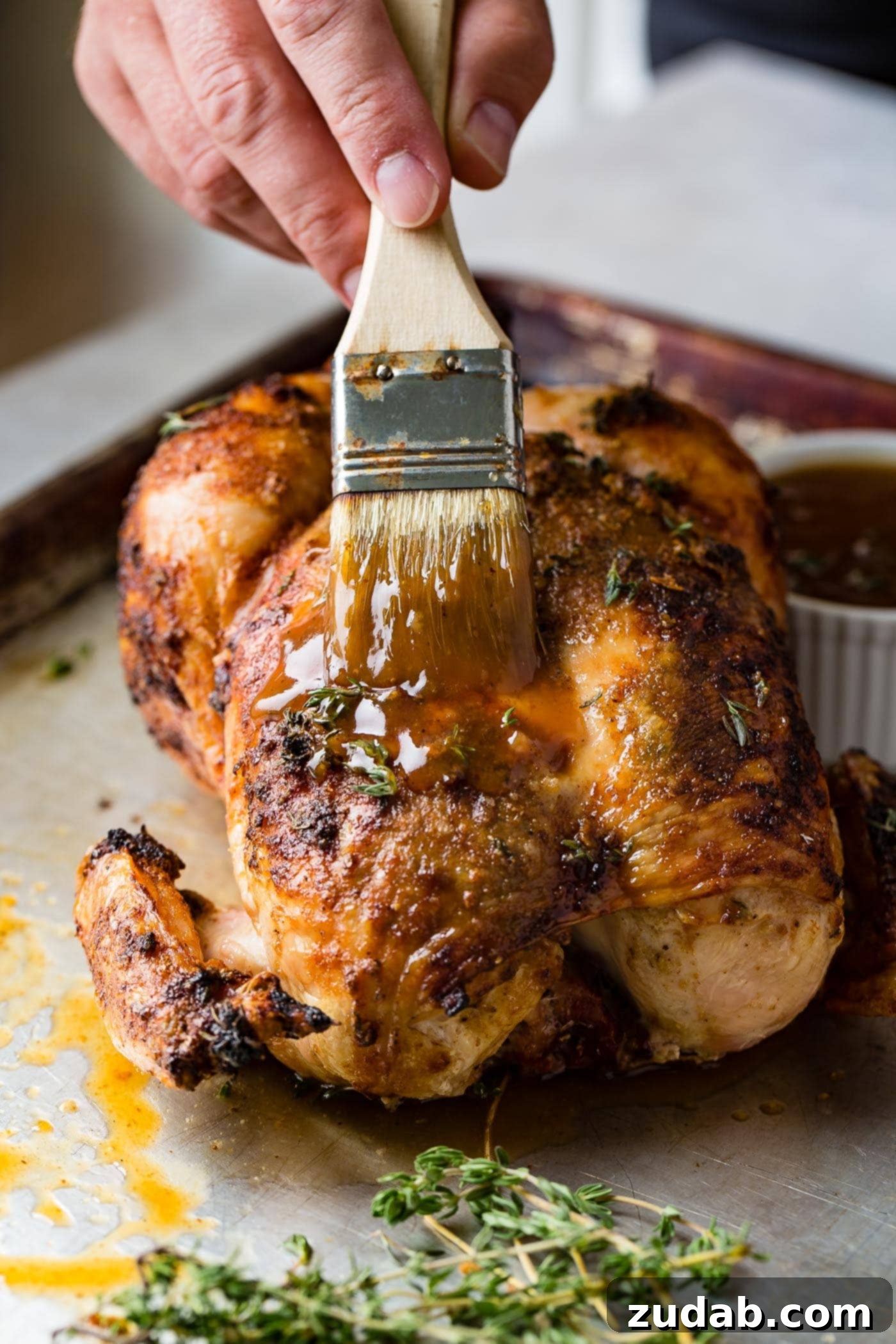 Traeger Smoked Whole Chicken 6 A flavorful glaze being brushed onto a whole smoked chicken, enhancing its rich color and creating a succulent finish. A small bowl of gravy and a dinner plate are ready in the background.