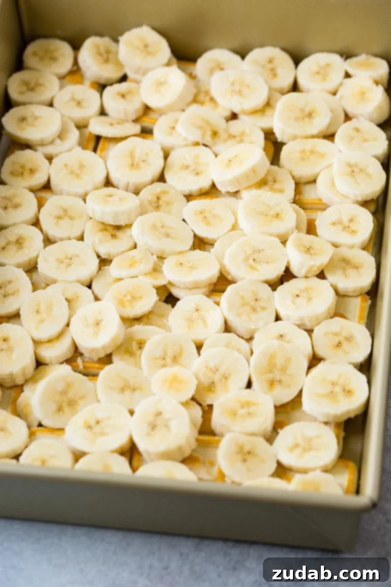 Paula Deen's Legendary Banana Pudding 5 A pan filled with a layer of freshly sliced ripe bananas, meticulously arranged over a bed of Chessman cookies. This layer forms the essential banana foundation for the creamy pudding, ensuring a burst of fruit in every bite.