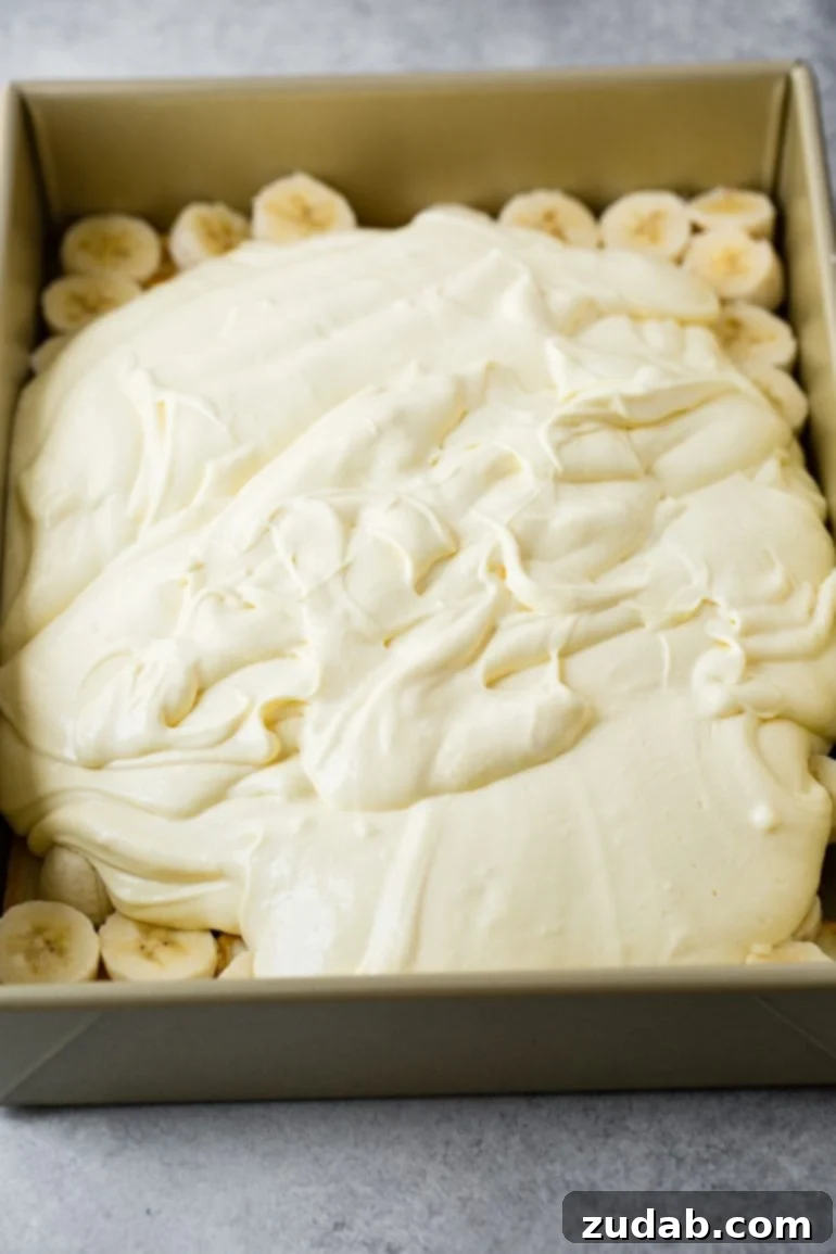 Paula Deen's Legendary Banana Pudding 6 A pan of banana pudding, where a smooth, creamy vanilla pudding mixture has been lovingly poured over the sliced bananas and cookie base. The pudding perfectly blankets the fruit, creating a tantalizing visual of layers that promise a delightful texture.