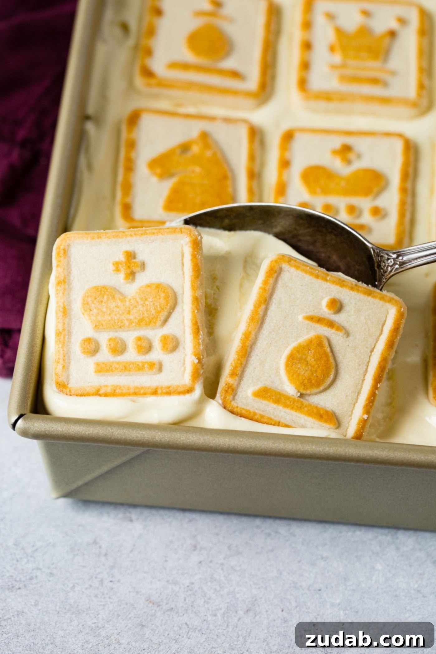 Paula Deen Banana Pudding A pan of creamy banana pudding, with a serving being elegantly scooped out by a spoon. The pudding appears light and airy, indicative of its fluffy texture, and is beautifully topped with yellow chess piece cookies, promising a delightful blend of flavors and textures in every bite.