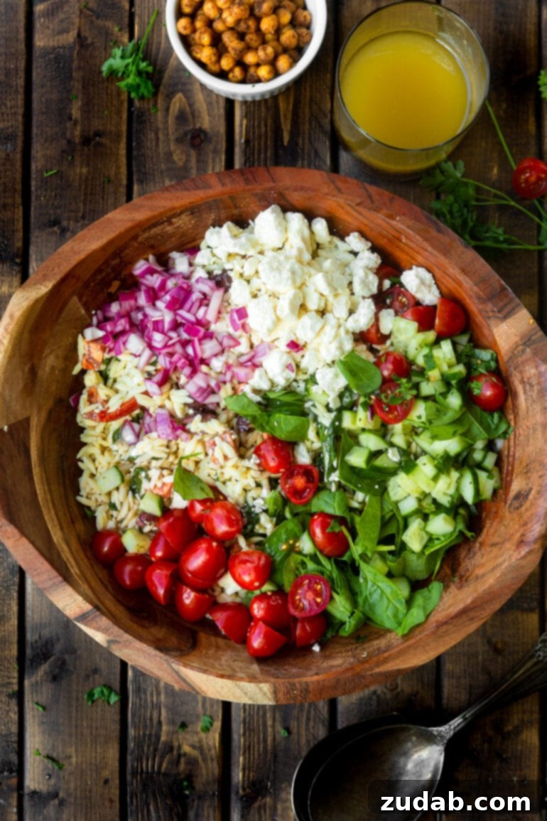 Zesty Mediterranean Orzo Salad 3 A high-angle photo displaying all the fresh, colorful ingredients for Greek orzo pasta salad neatly arranged in a large wooden serving bowl before being tossed.