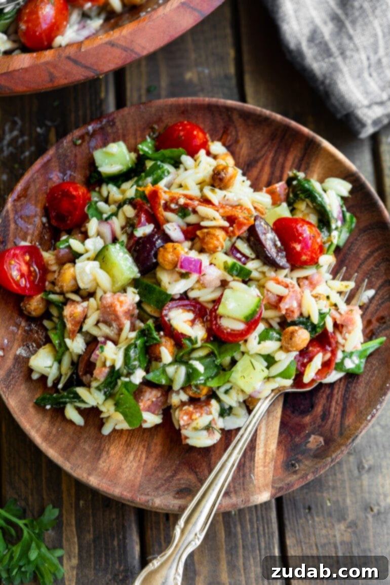 Zesty Mediterranean Orzo Salad 5 A close-up photo of a single serving of Greek orzo pasta salad on a rustic wooden plate, with a fork digging into the salad, ready to be enjoyed.