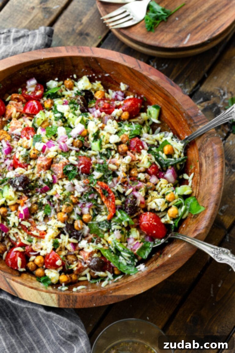 Zesty Mediterranean Orzo Salad 7 A large wooden serving bowl filled with Greek orzo salad, featuring two wooden serving spoons nestled within, ready for sharing.