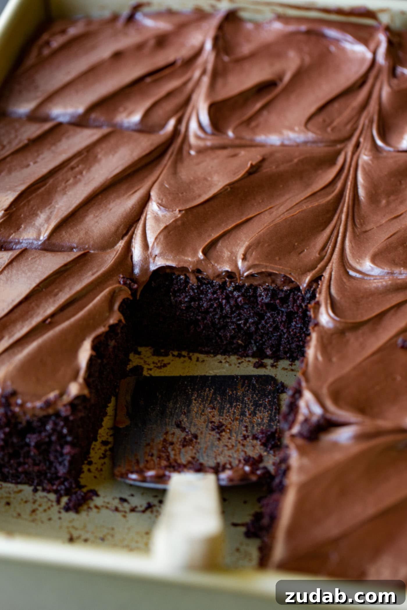 Moist Chocolate Zucchini Cake A pan of moist chocolate zucchini cake, cut into generous pieces, with one slice removed to reveal its rich, chocolatey interior. Each piece is topped with smooth, creamy chocolate cream cheese frosting.