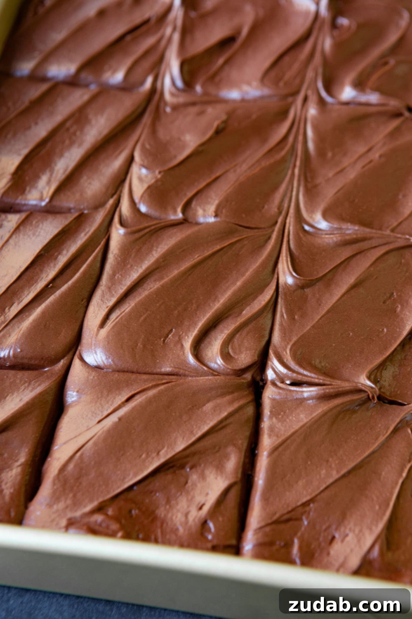 Moist Chocolate Zucchini Cake A beautiful top-down view of a moist chocolate zucchini cake, generously covered in a swirl of chocolate cream cheese frosting. The cake has been sliced into portions, ready to be served.