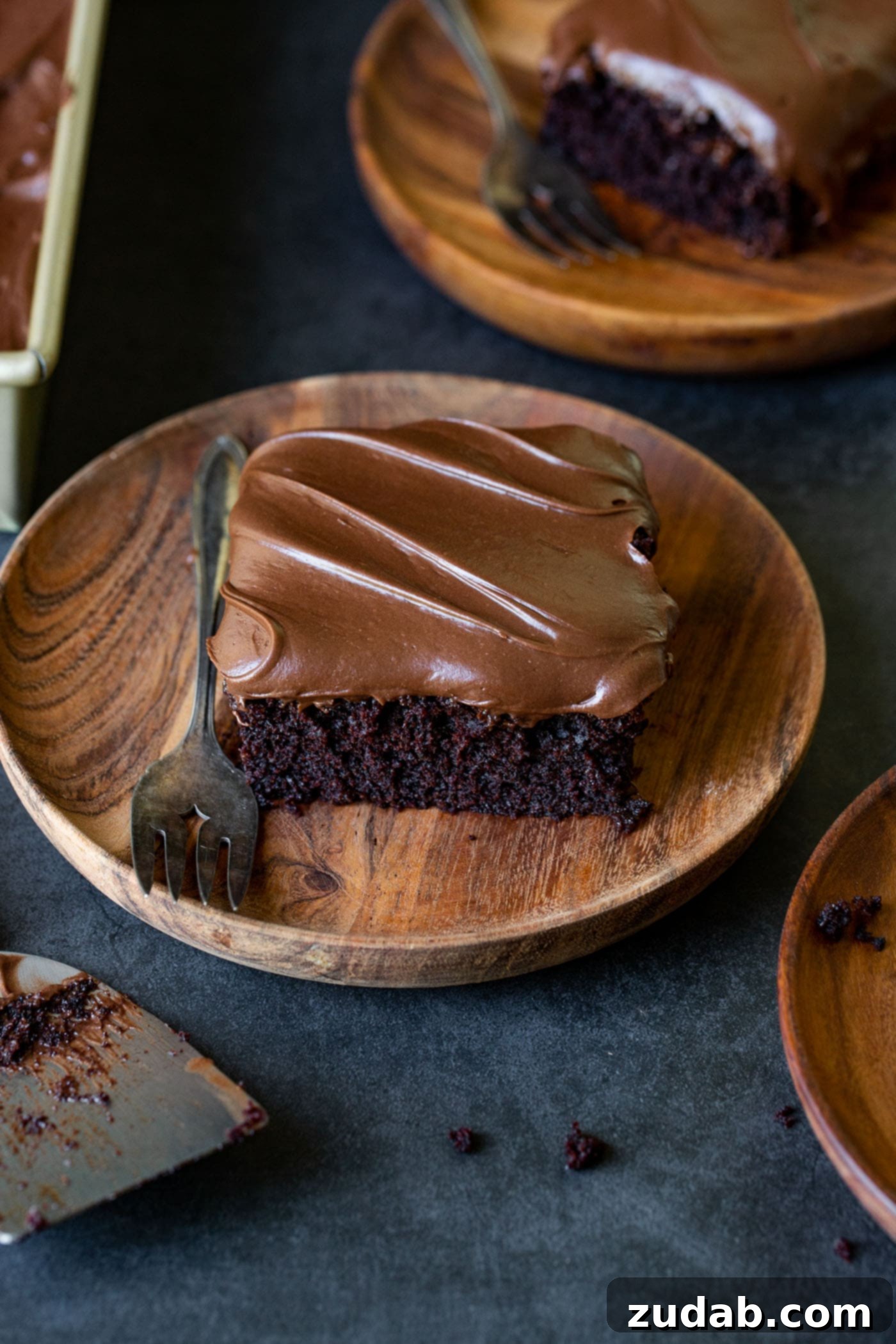 Moist Chocolate Zucchini Cake A delightful arrangement of moist chocolate zucchini cake slices on wooden dessert plates, accompanied by a fork. The focus highlights the rich, chocolatey, and moist interior of the cake, with creamy frosting visible.