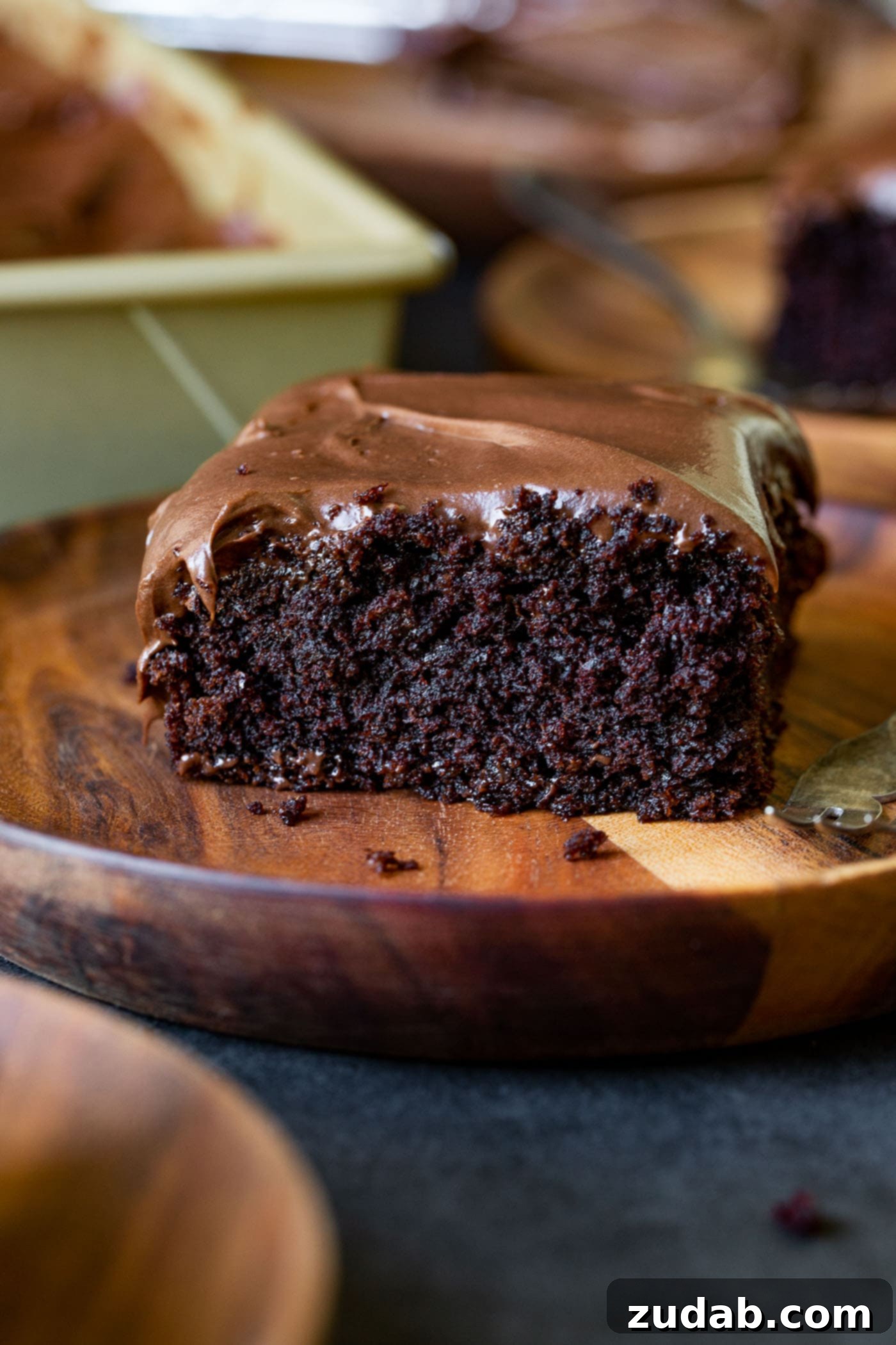 Velvet Chocolate Zucchini Cake 3 A perfect slice of moist chocolate zucchini cake, adorned with luxurious chocolate cream cheese frosting, elegantly placed on a wooden dessert plate. It beckons with its rich texture and enticing flavor.