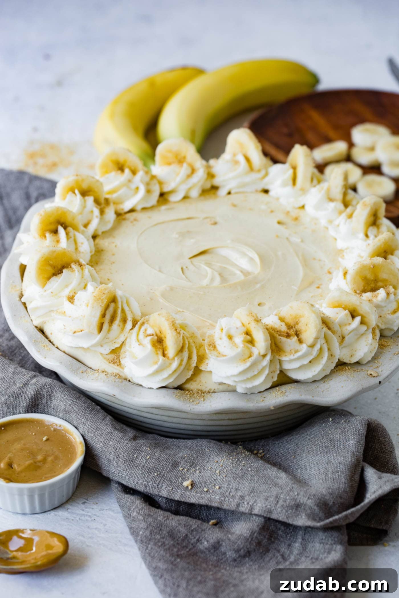 Peanut Butter Banana Cream Pie A peanut butter banana cream pie with whipped cream and bananas around the edge. There are bananas and peanut butter in the background.