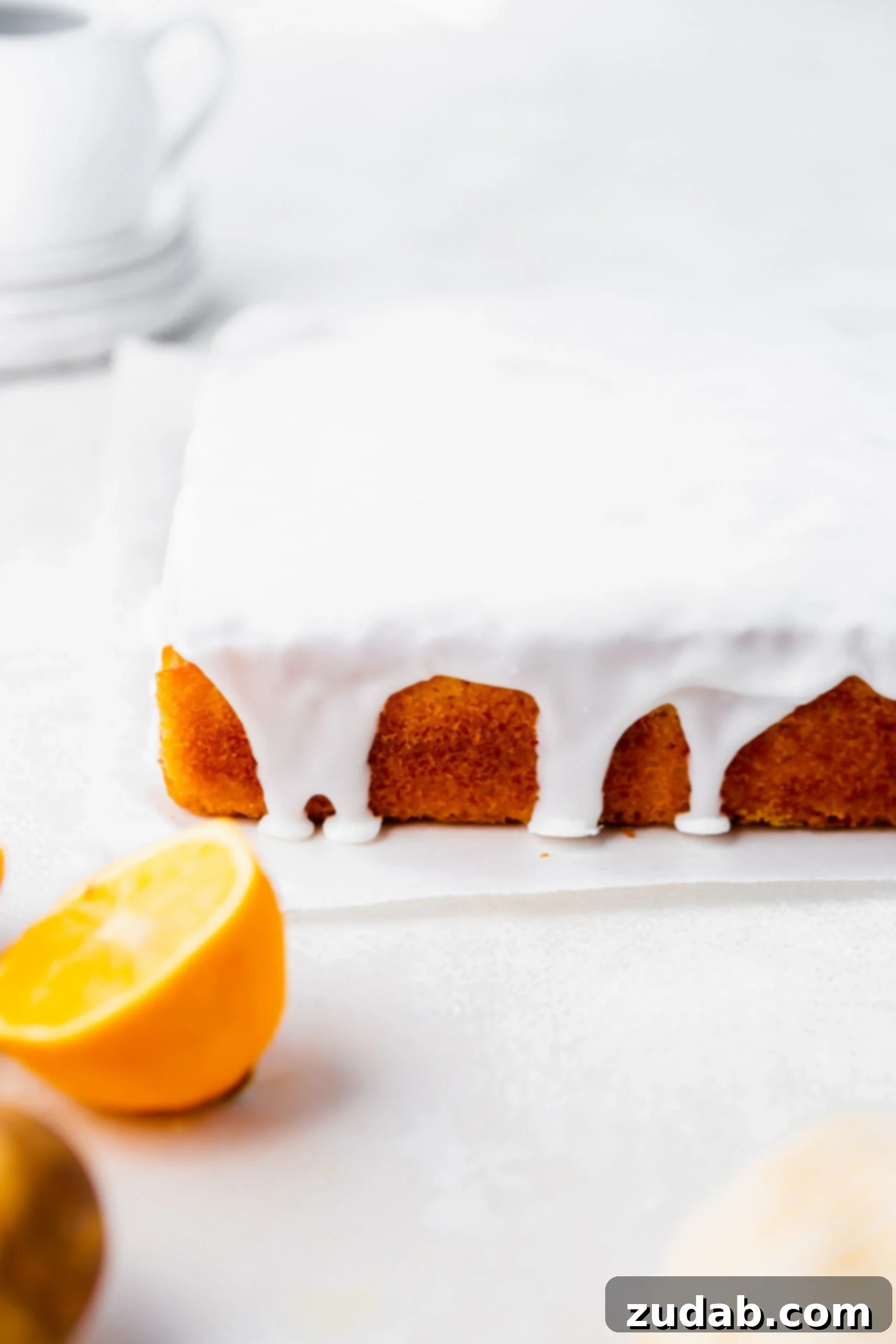 Zesty Glazed Lemon Treat 3 A square lemon cake, beautifully draped in a thick, shiny white lemon glaze that gracefully drips down its sides.