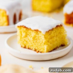 Zesty Glazed Lemon Treat 4 a photo of one piece of lemon cake topped with white frosting and sitting on a white plate. Several servings of cake are in the background.