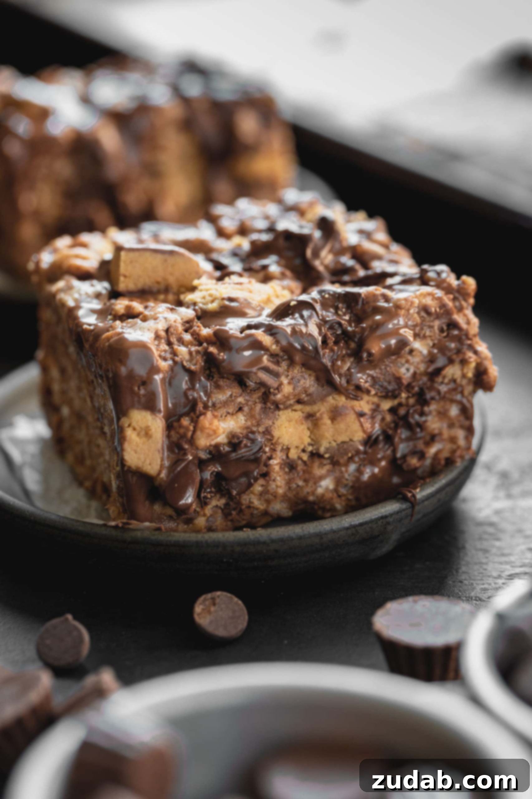 Reese's Rice Krispies Treats A photo of a rice krispies treat loaded with Reese's Peanut Butter Cups and melted chocolate chips on a small plate, with additional chocolate chips and mini Reese's cups in the foreground.
