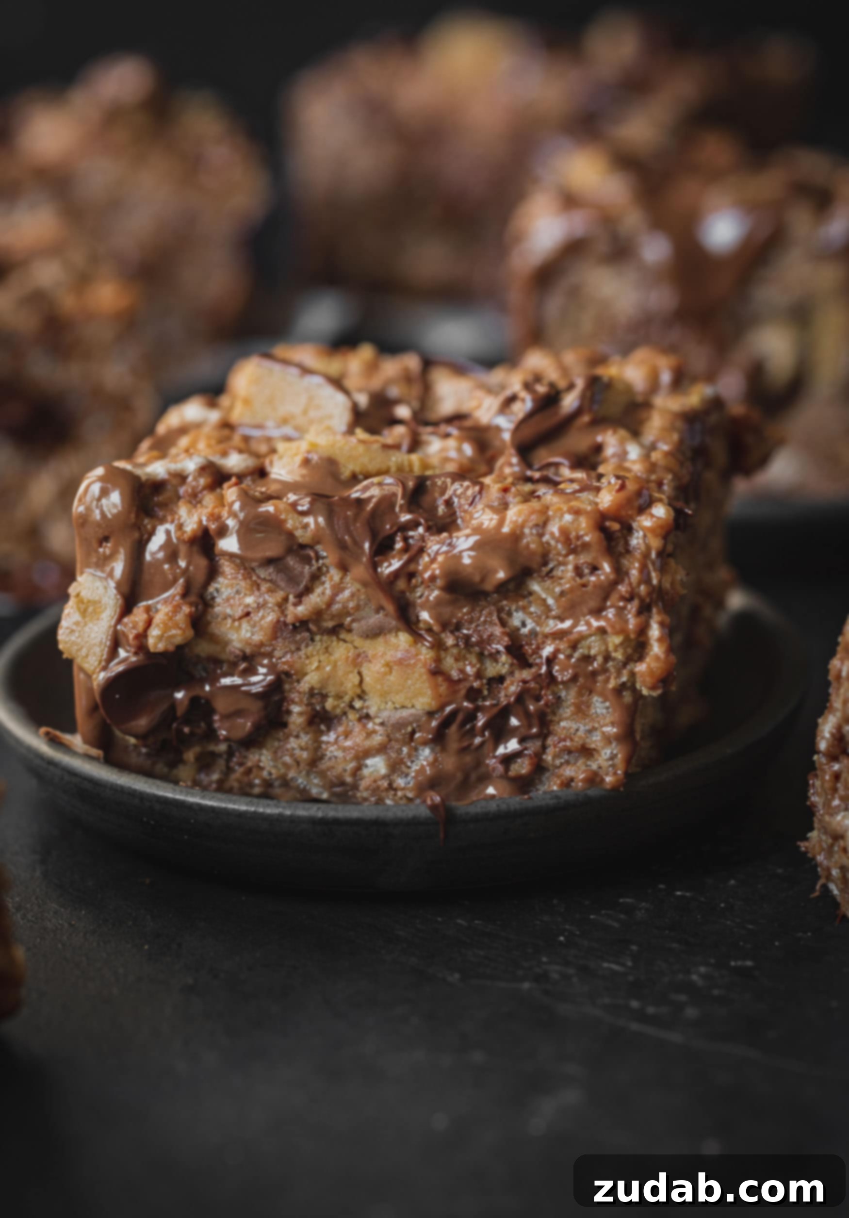 Reese's Rice Krispies Treats A photo of a single peanut butter rice krispies treat loaded with Reese's Peanut Butter Cups and melted chocolate chips on a dark gray plate, with several more rice krispies treats in the background.