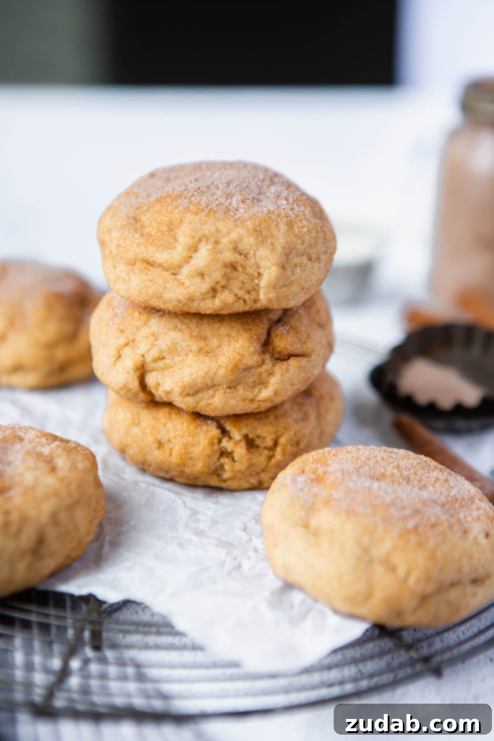 Serving Thick Snickerdoodle Cookies Three perfectly baked thick, fat snickerdoodles are stacked majestically on top of each other, showcasing their impressive height and inviting texture. More delicious snickerdoodles are visible in the background, ready for enjoyment.